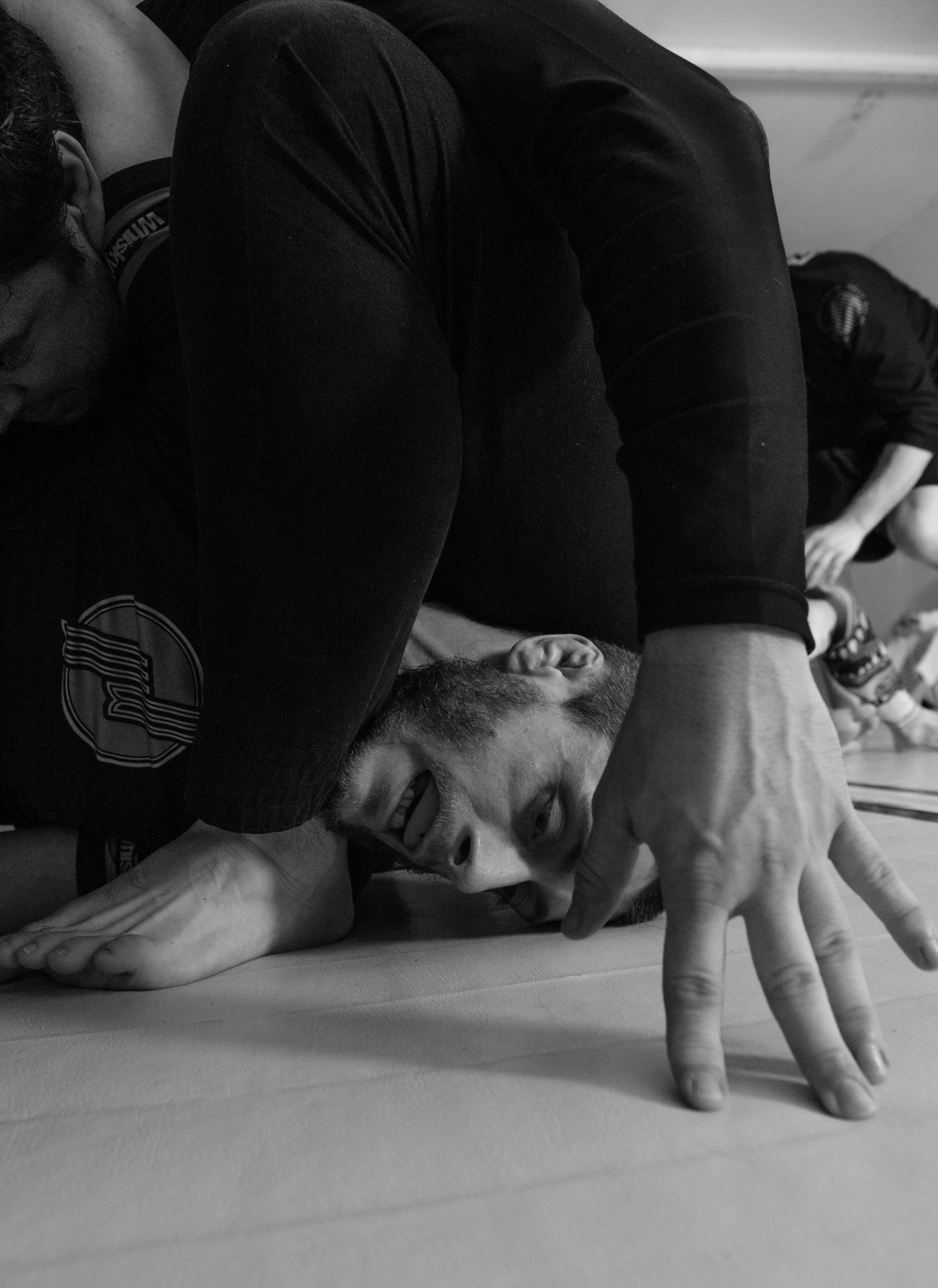 A person in black training gear practices Brazilian Jiu-Jitsu moves on a white mat during a grappling session.