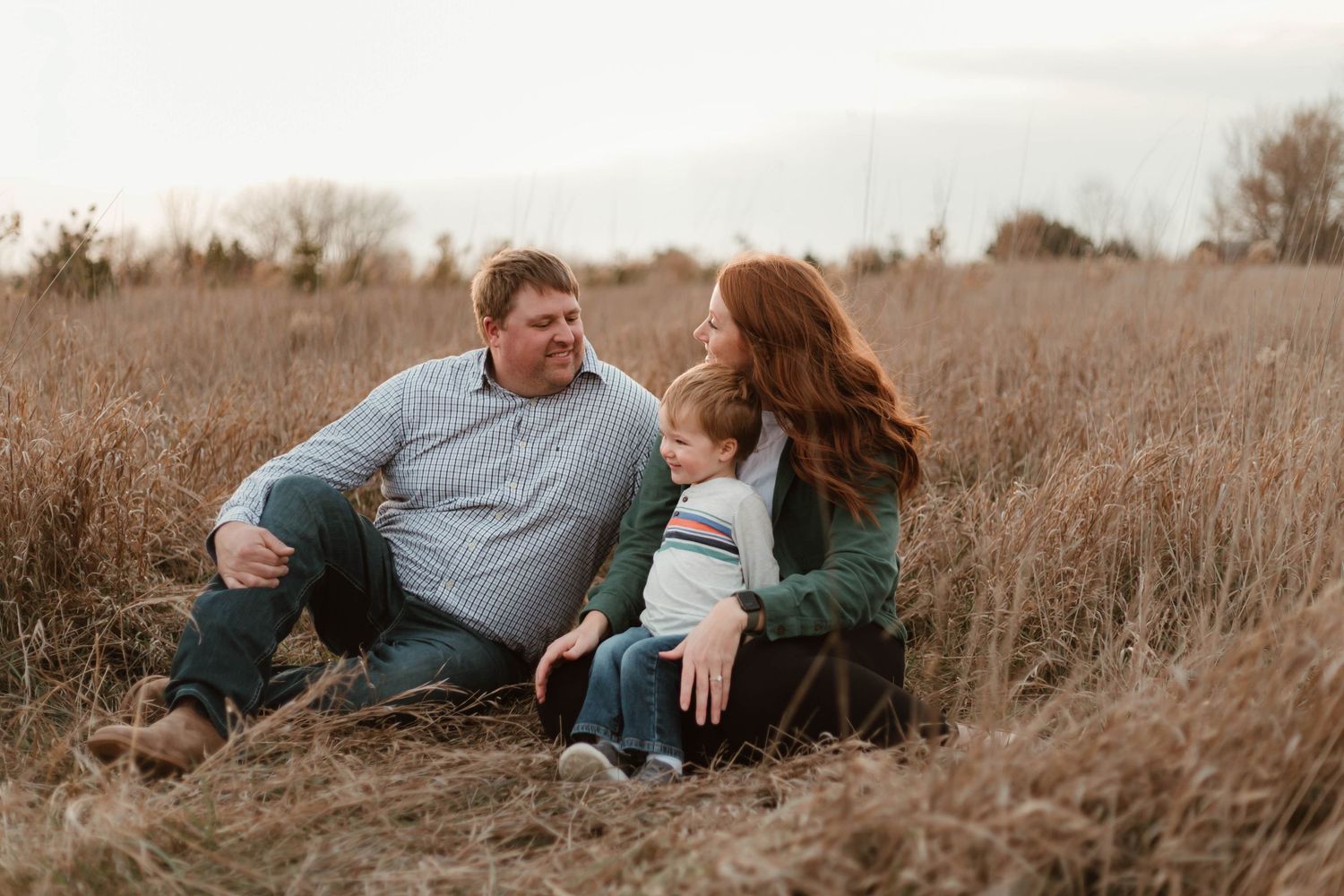 Family of three cuddling in grassy field Southeast Minnesota