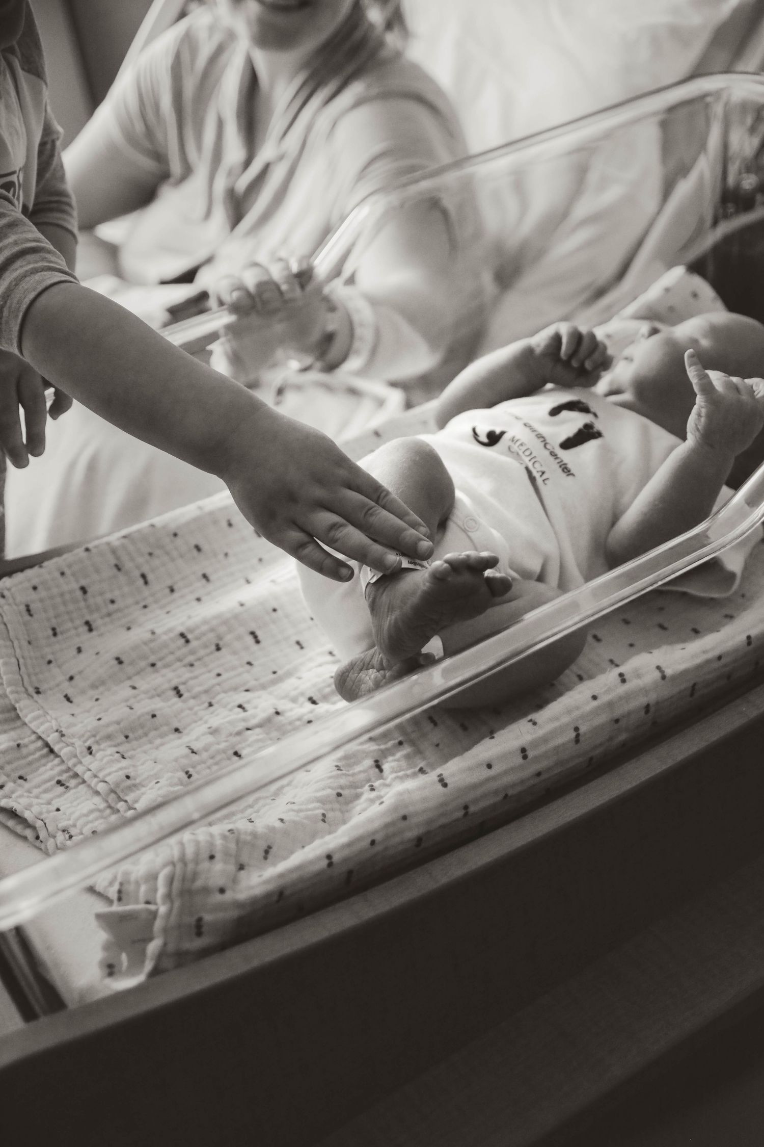 Hands of mom and big brother in bassinet of new baby brother in hospital in Southeast Minnesota