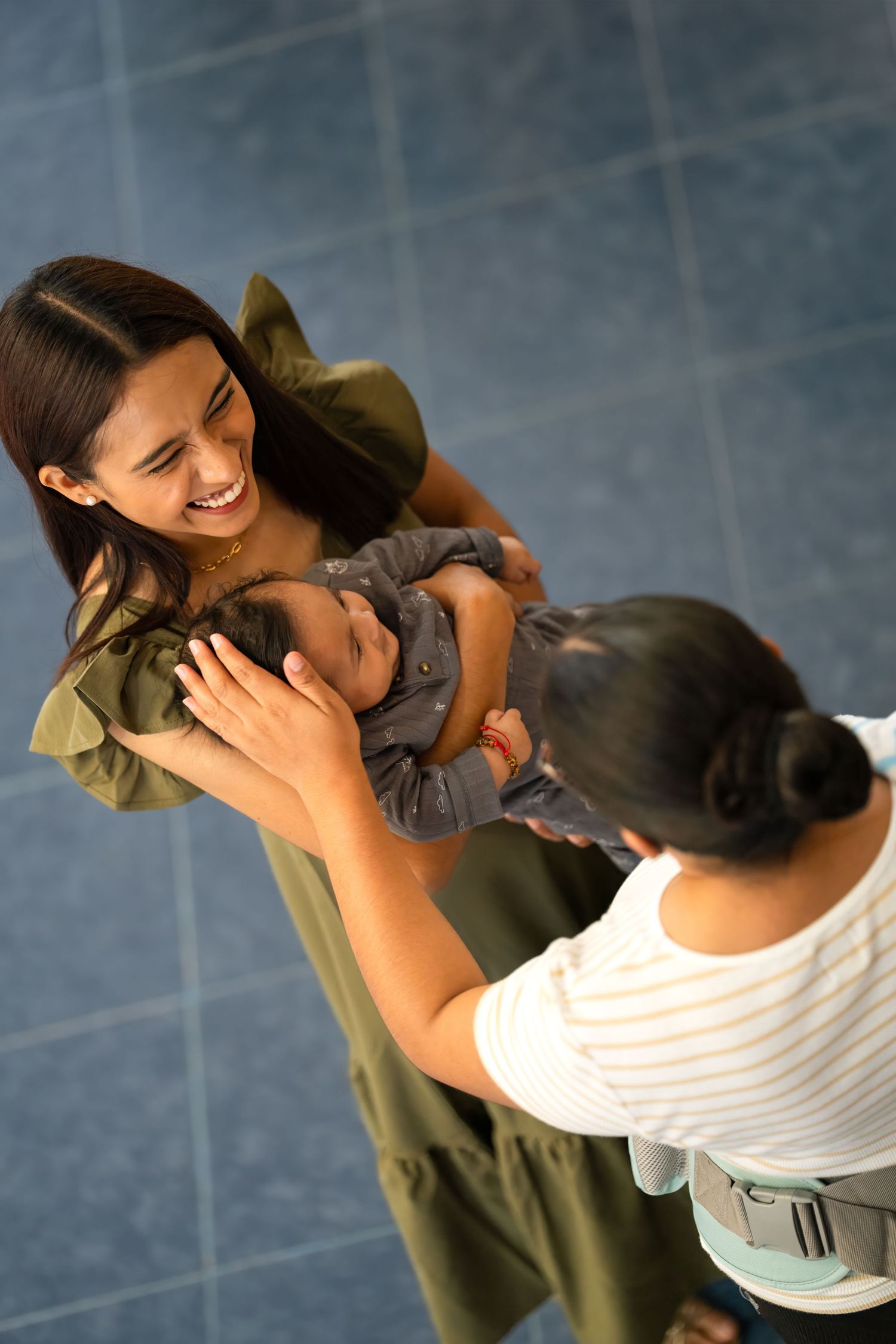 Overhead view of a mother smiling while holding her baby as another adult reaches in affectionately.