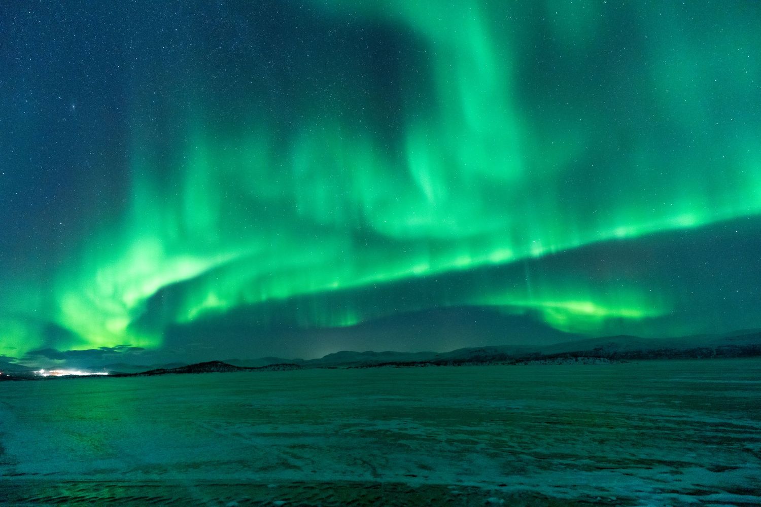 Green northern lights stretching across a winter night sky above snow-covered mountains in northern Sweden.