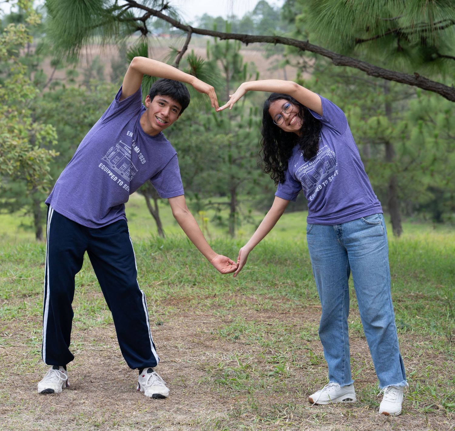Two students smiling and forming a heart shape with their arms during an outdoor portrait session.