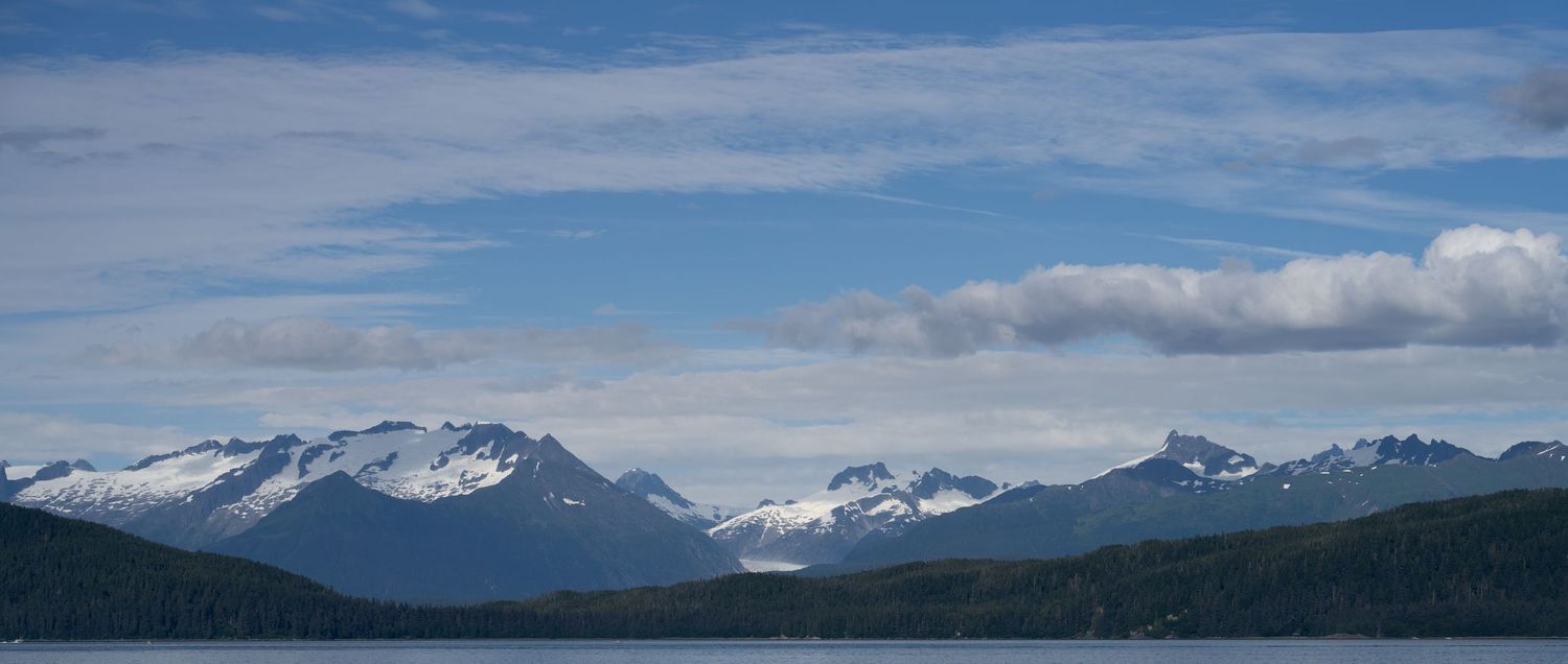 Panoramic Alaskan mountain landscape with snow-capped peaks under a blue sky.