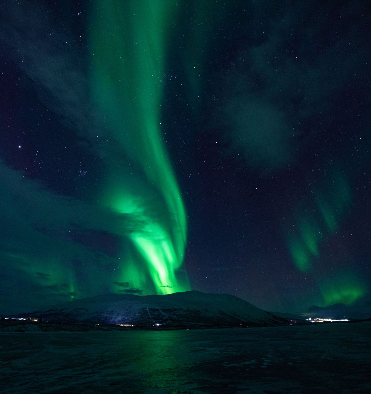 Northern lights illuminating the night sky above dark mountains and a frozen landscape.