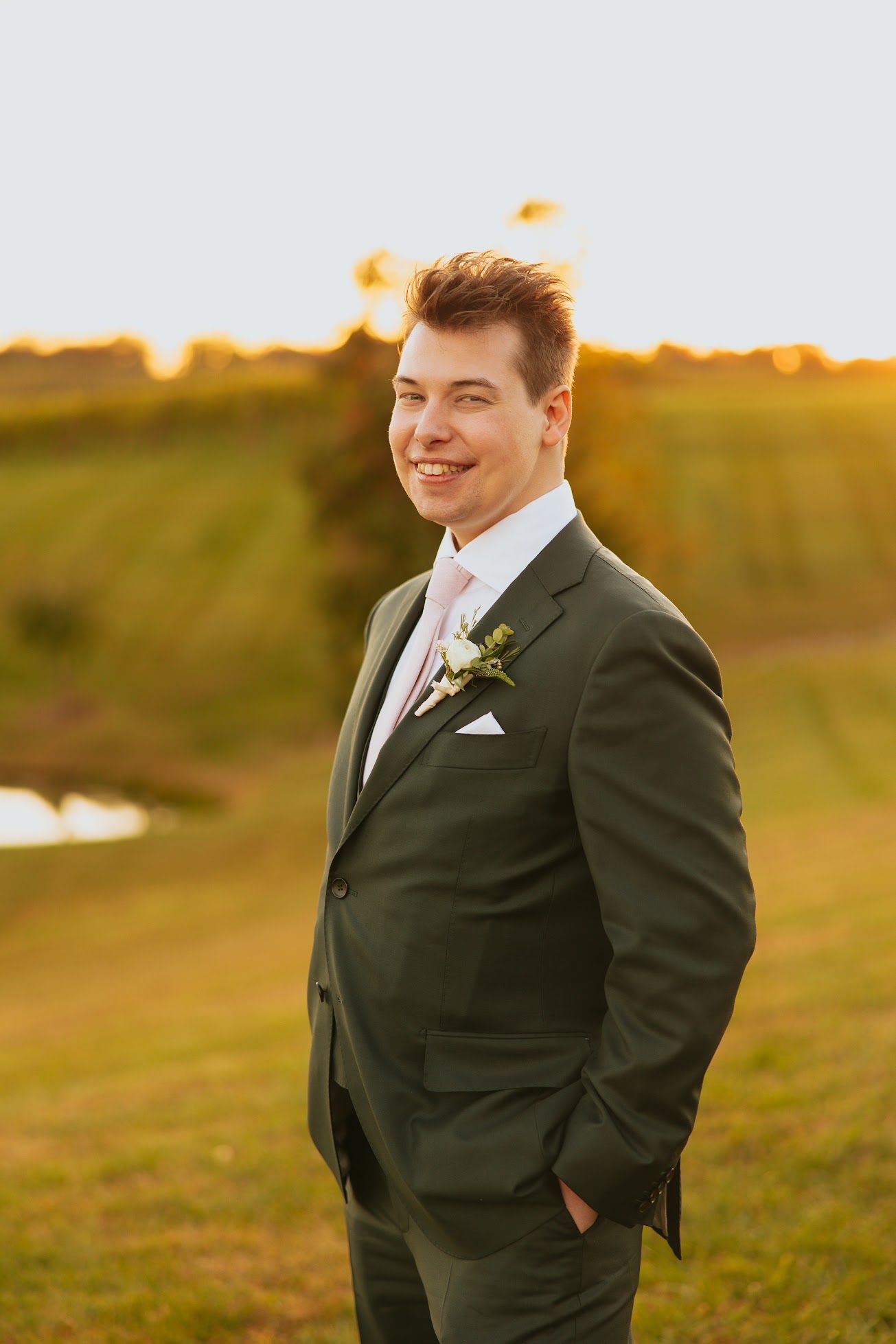 Outdoor portrait of a Alexander Mann in a green suit standing in a field during golden hour at sunset.