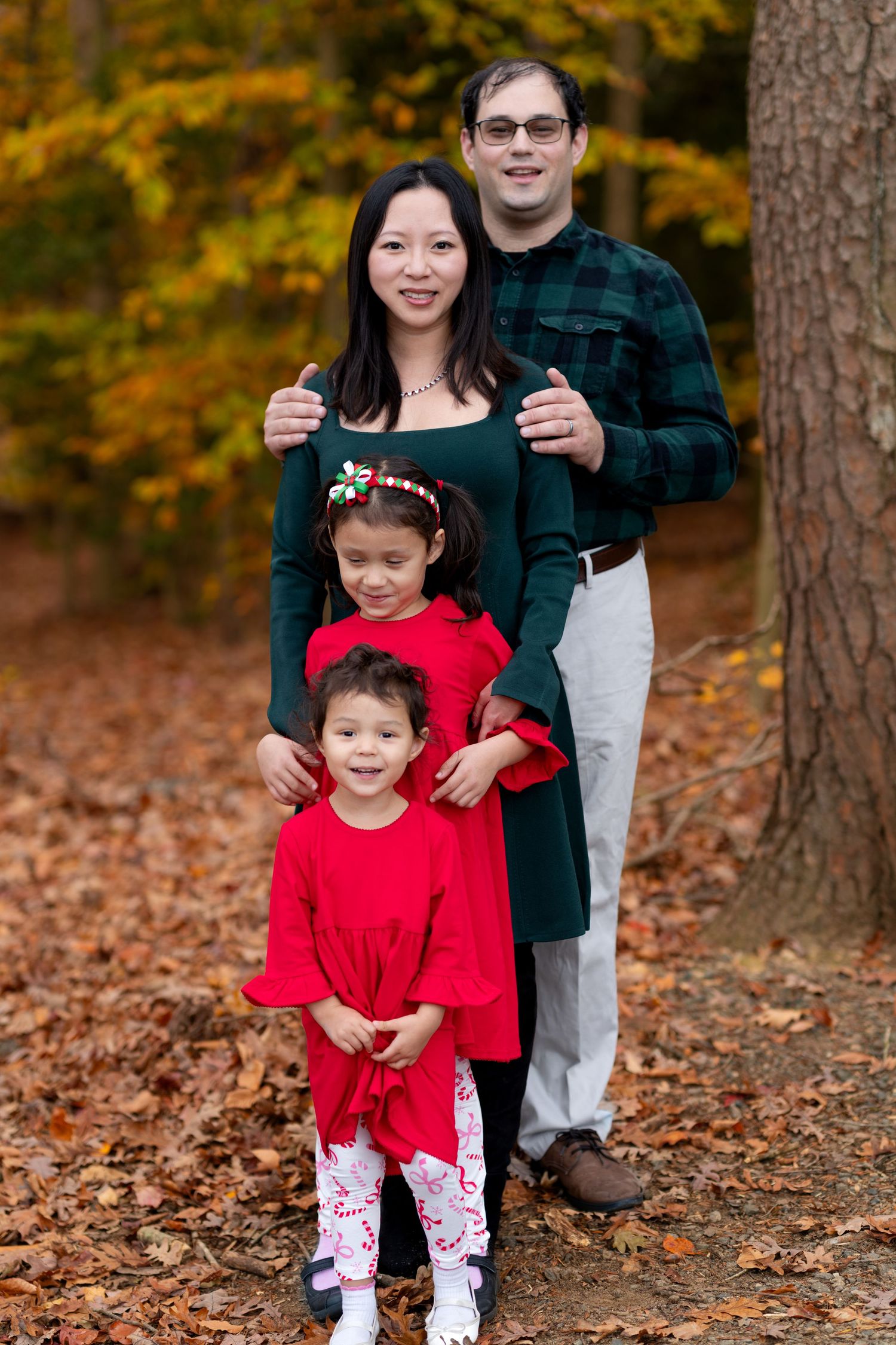 Outdoor family portrait of parents and children standing together in an autumn forest with fall foliage in the background.