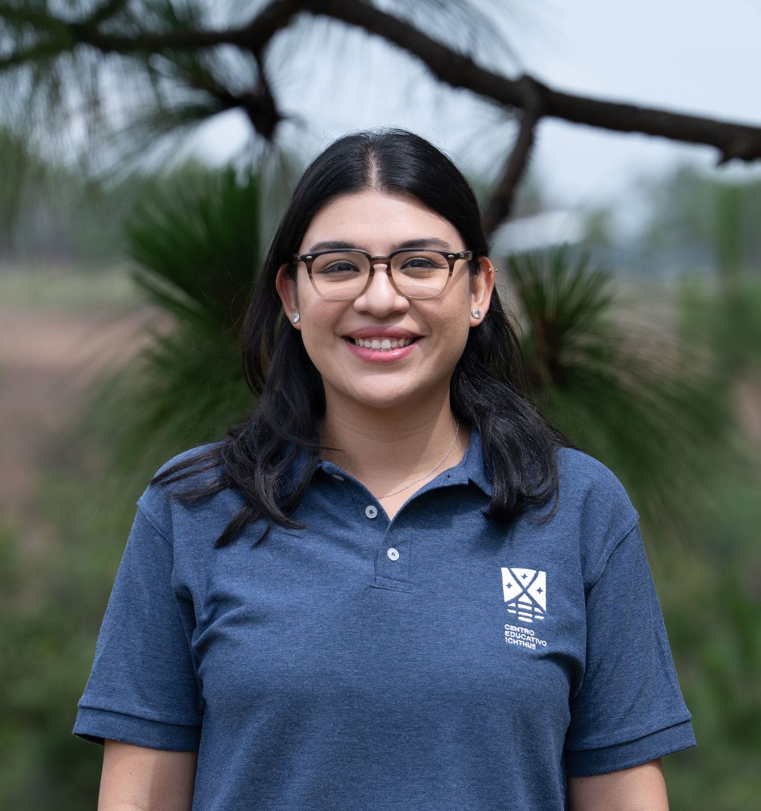 Professional outdoor headshot of a woman smiling, wearing glasses and a branded polo shirt.