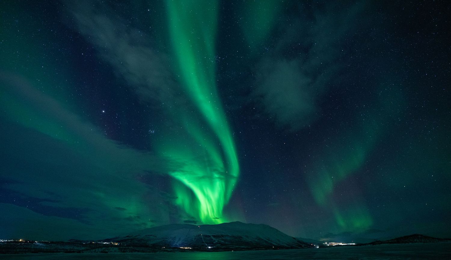 Northern lights illuminating the night sky above dark mountains and a frozen landscape.