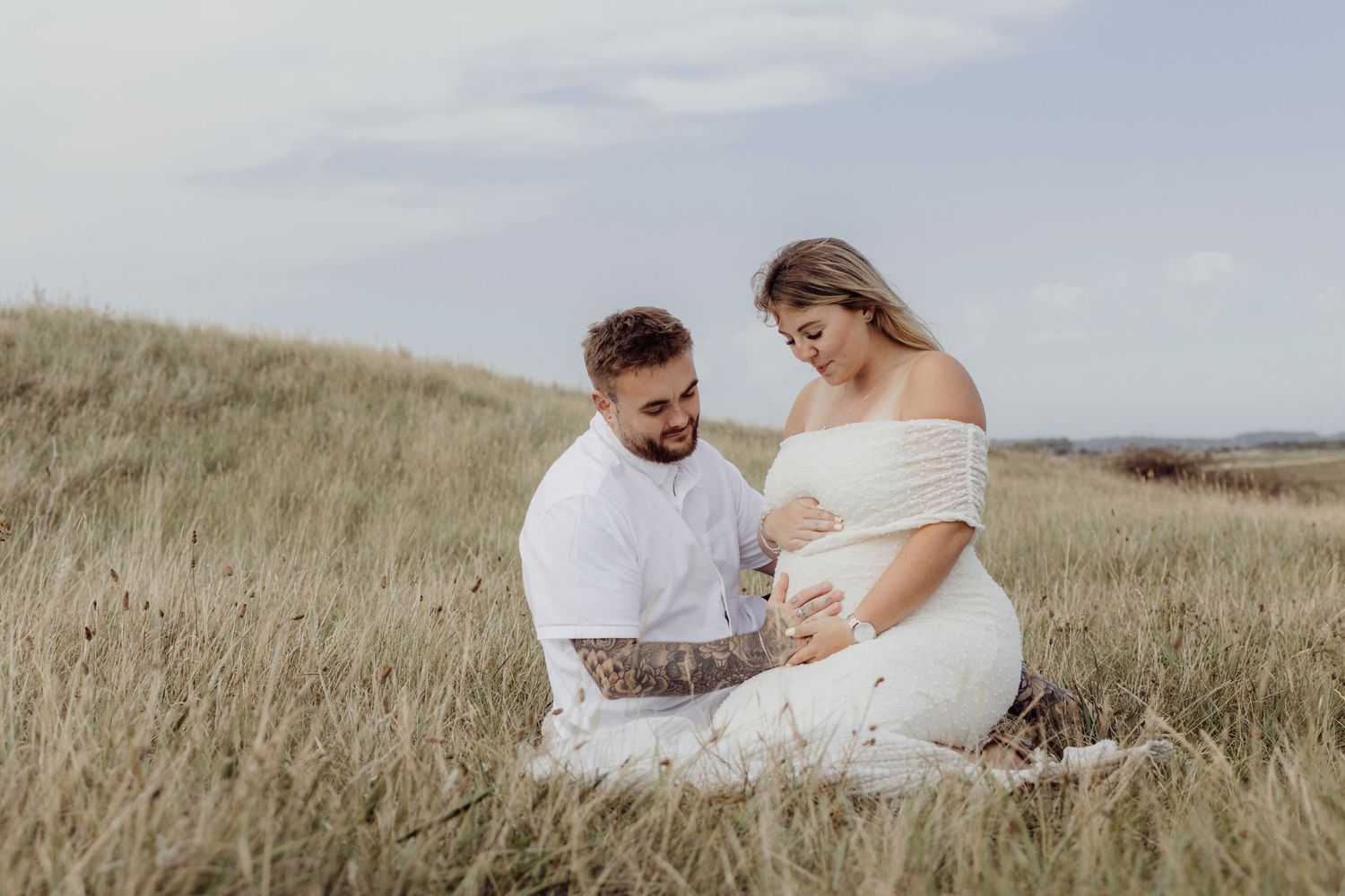 A couple embraces on a grassy hillside in an intimate outdoor photoshoot at sunset.