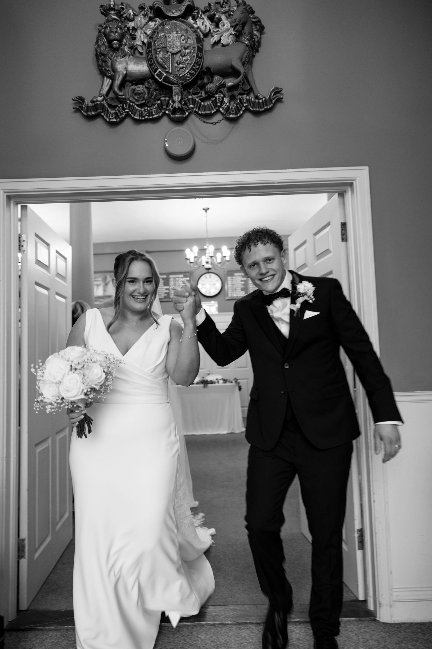 A black and white photo of a wedding party walking through an elegant corridor.