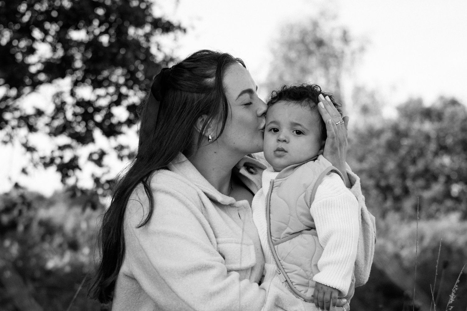 A tender black and white portrait of a parent and child sharing an intimate moment outdoors.