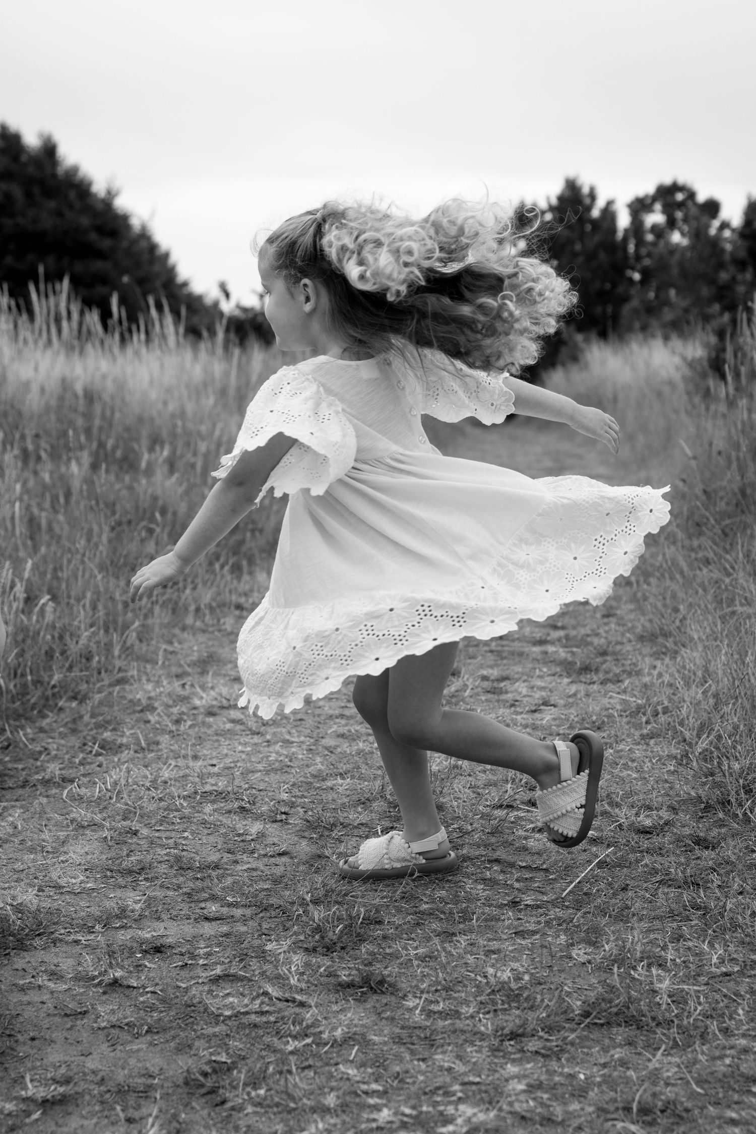 Child in white dress twirling and playing in a grassy field at sunset.