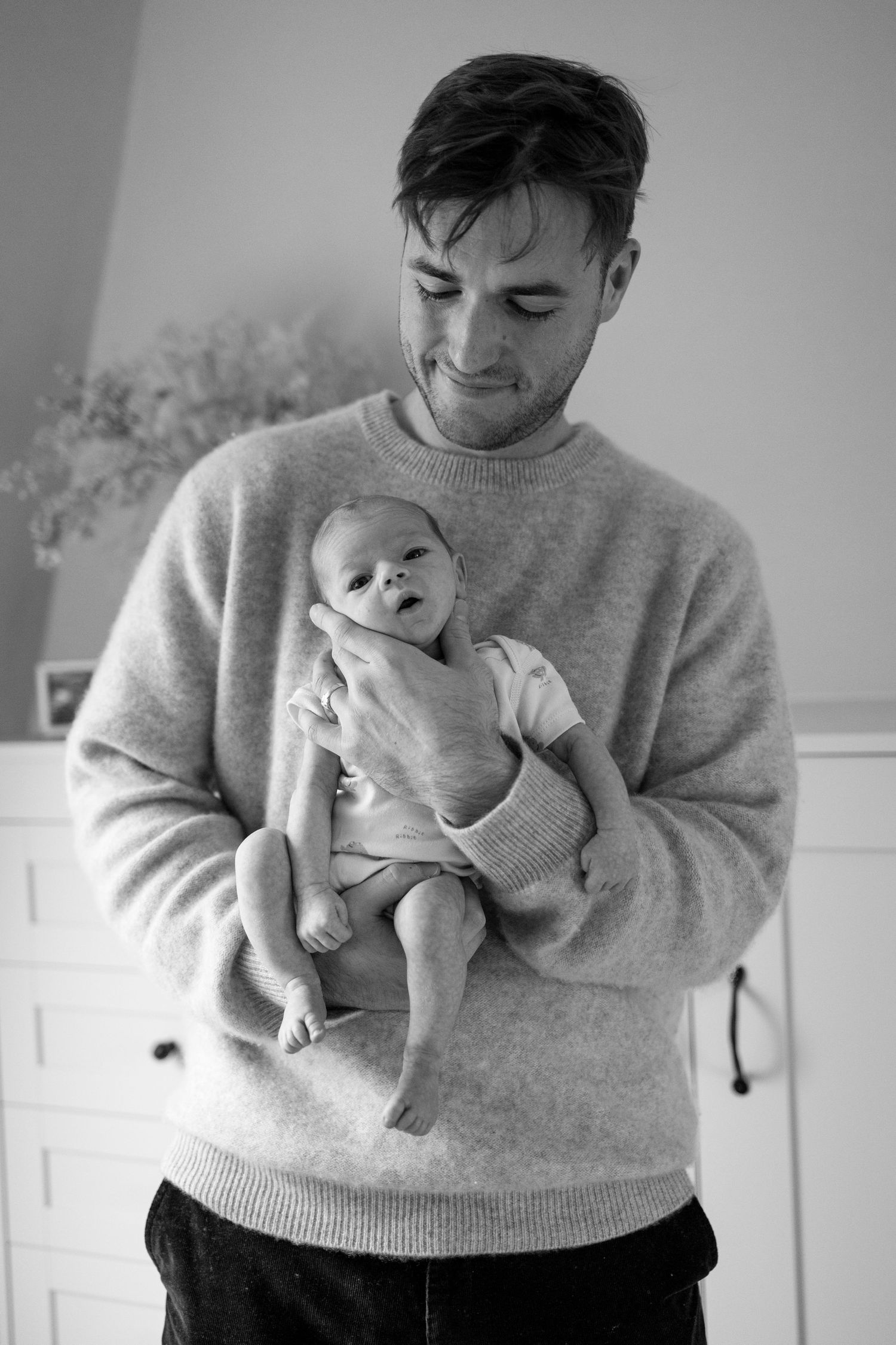A person in a gray sweater holds and gazes lovingly at a newborn baby in a series of tender black and white photos.
