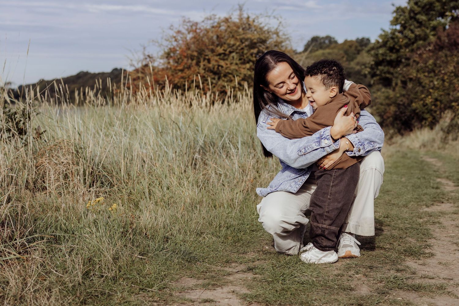 Mother and child play together along a natural path surrounded by autumn vegetation.