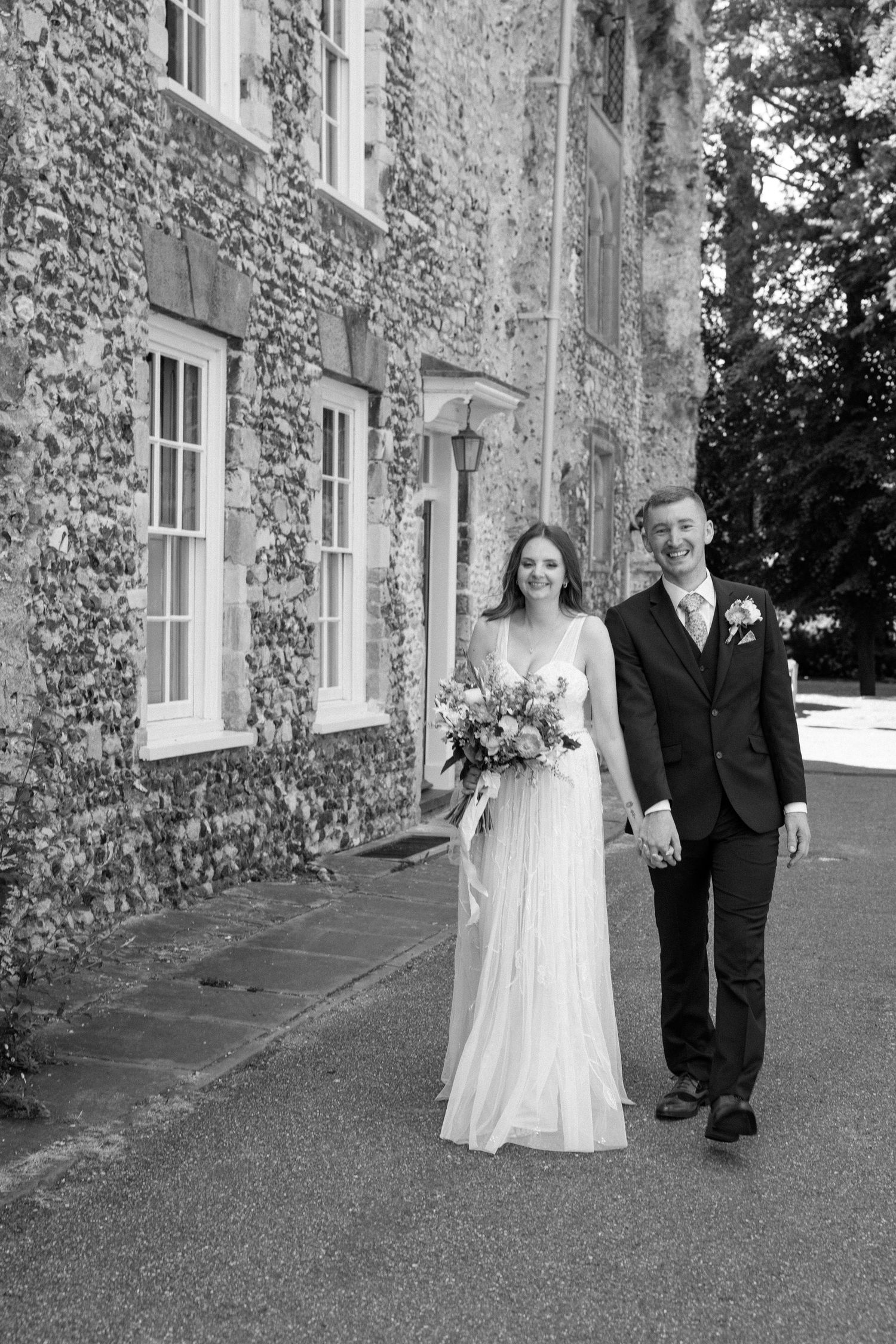 A bride and groom pose together against an ivy-covered stone building.