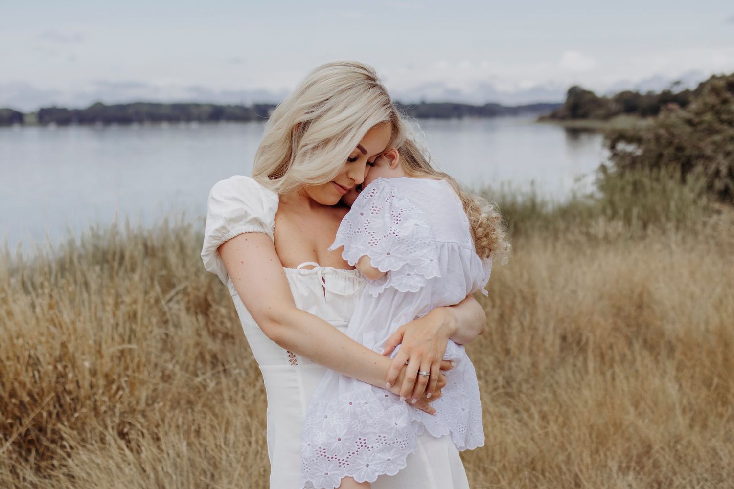 Intimate family moment captured in golden light against tall grass and water backdrop.