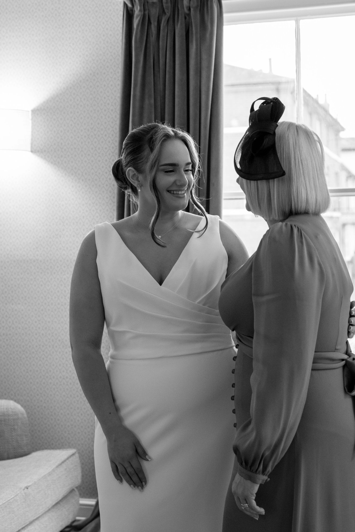 A bride in a white V-neck wedding dress getting ready in a sunlit room.