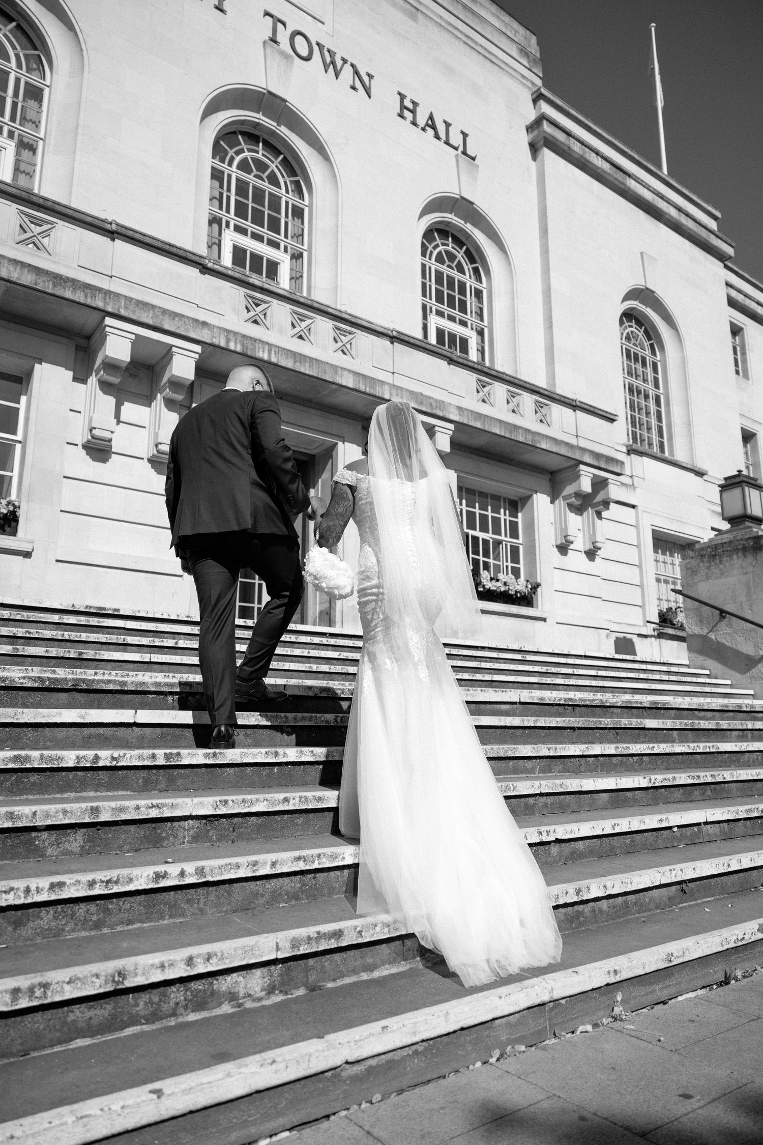 A couple ascends the grand steps of a historic town hall building on their wedding day.