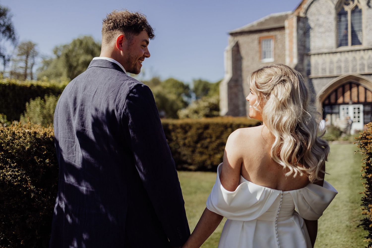 A couple in wedding attire stands together on the grounds of a historic building.