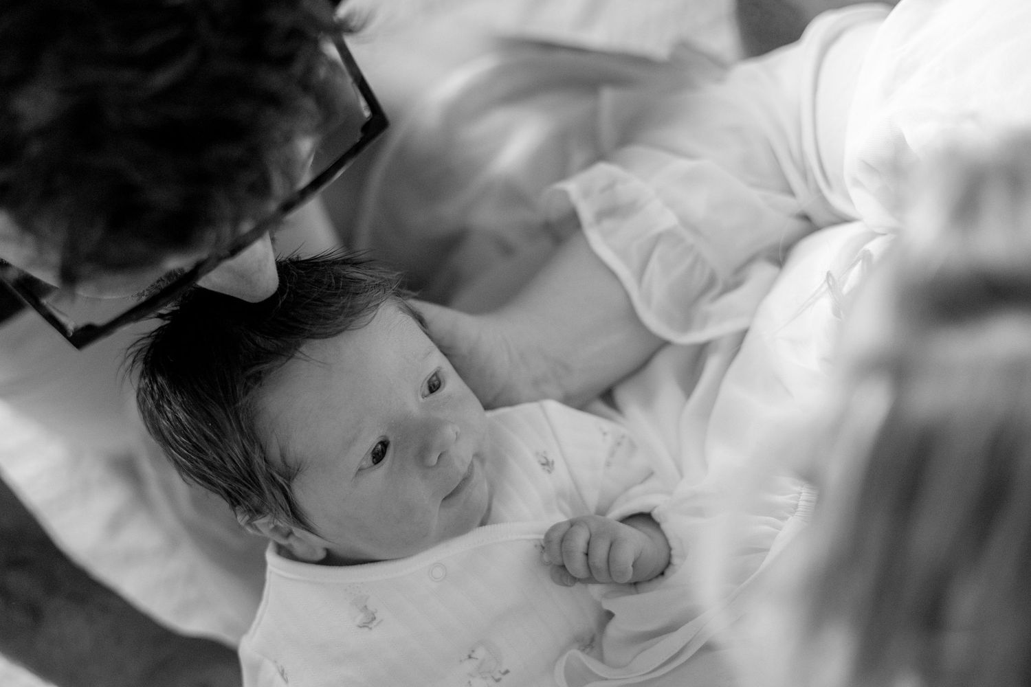 Black and white photo of a newborn baby being held by parents during a tender family moment.