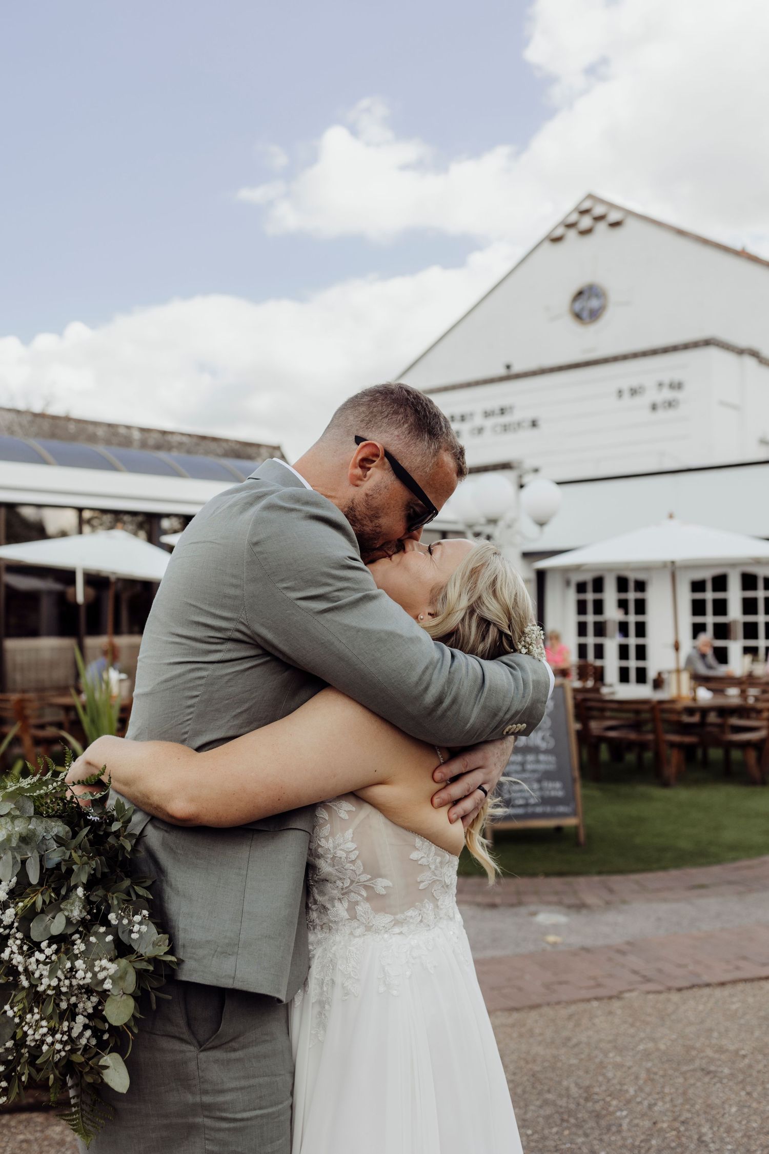 A tender embrace between a couple in wedding attire outside a rustic white venue.