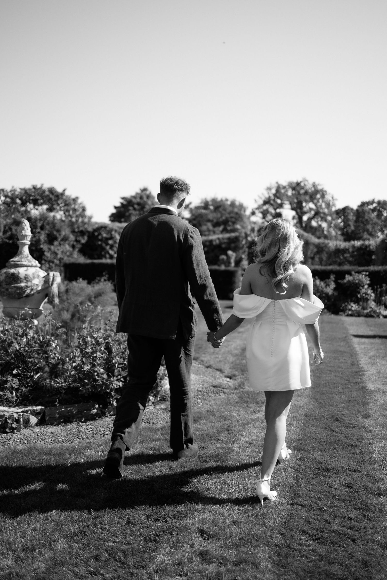 Newlyweds walk hand in hand through a garden path on their wedding day.