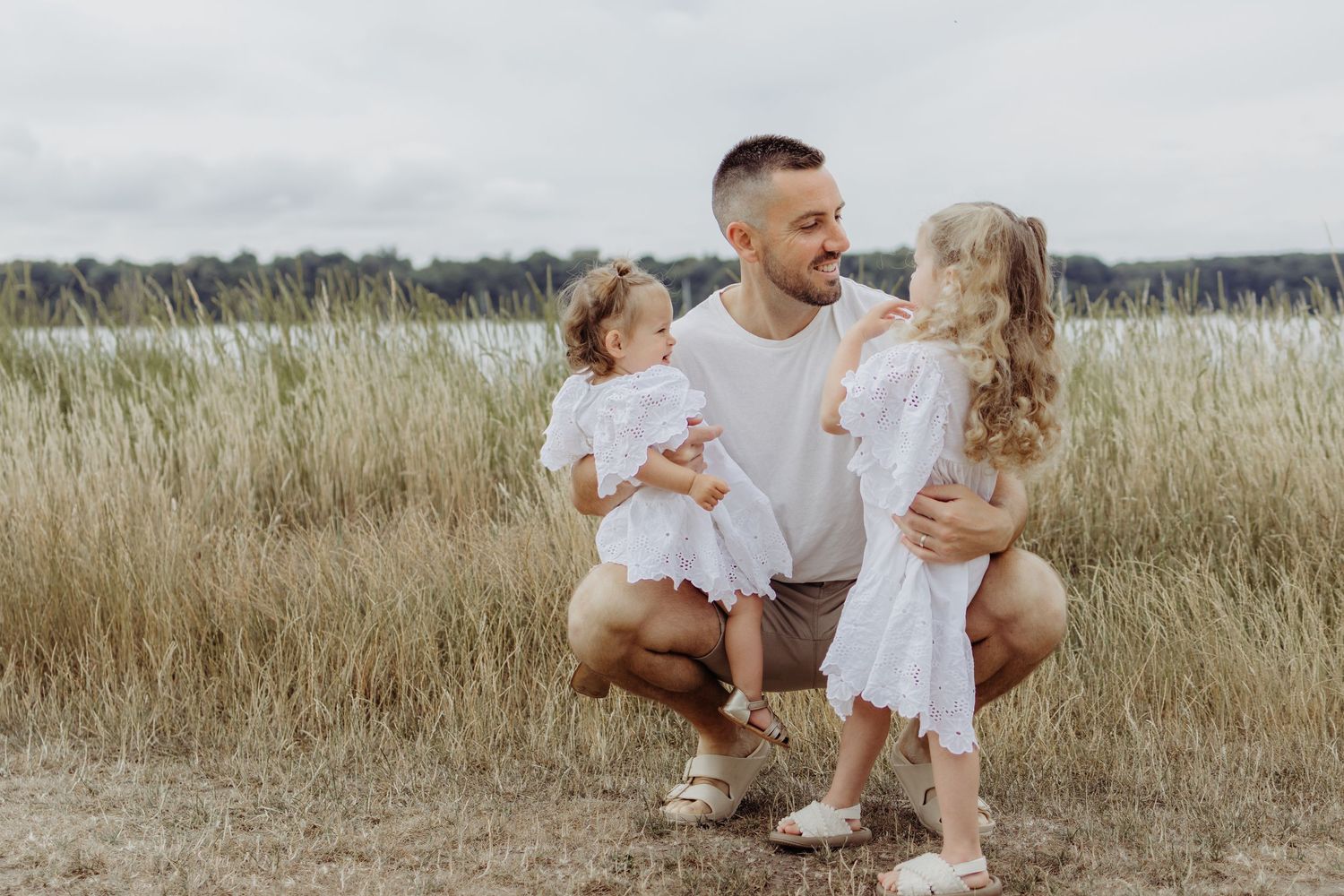 A family in white outfits plays together in a sunlit grassy meadow on a summer day.