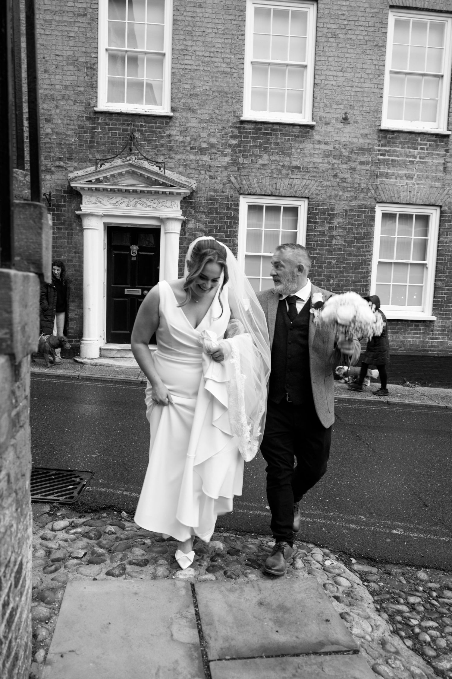 A wedding couple sharing joyful moments outside a traditional brick building.