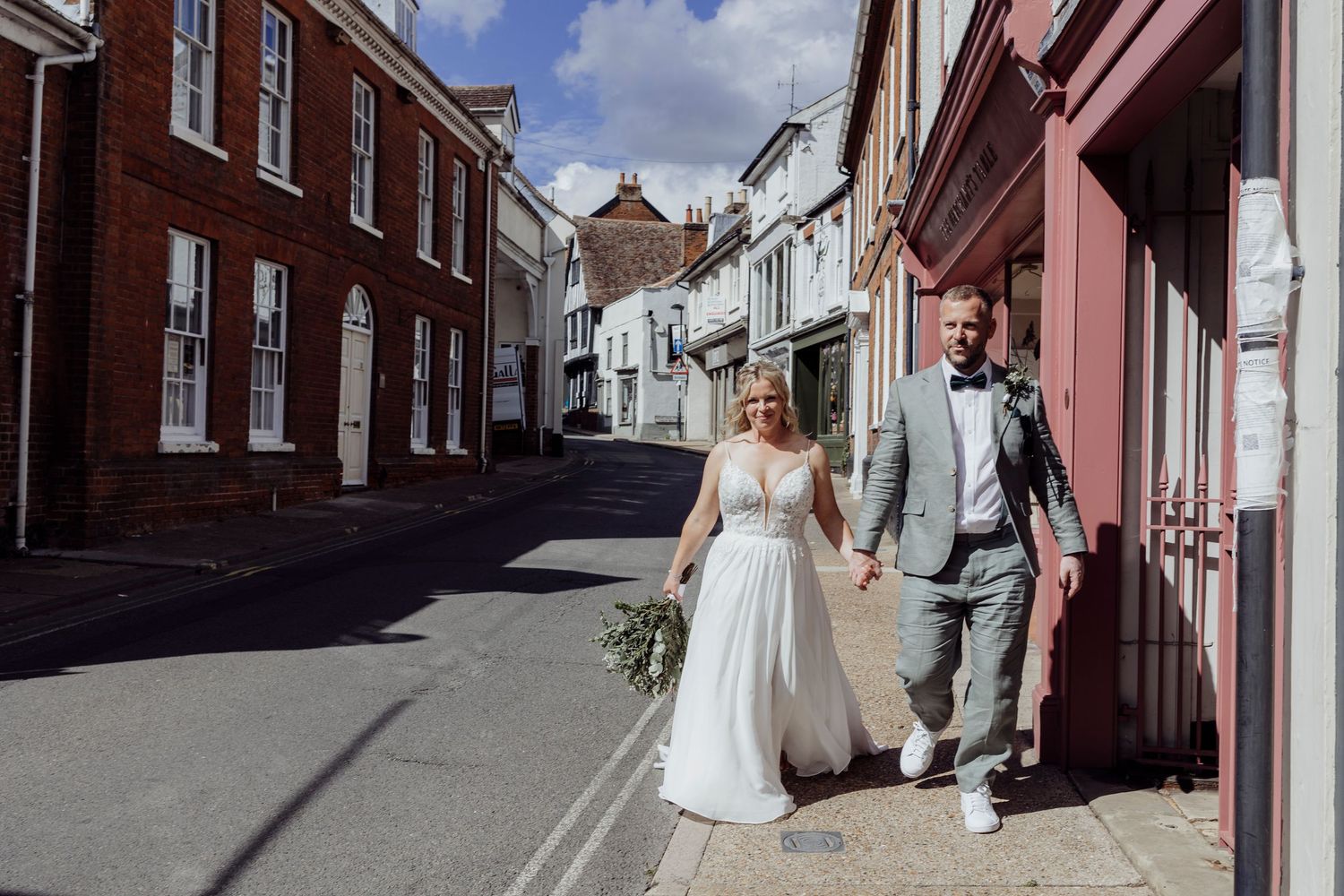A couple walks hand in hand down a charming cobblestone street lined with red brick buildings.