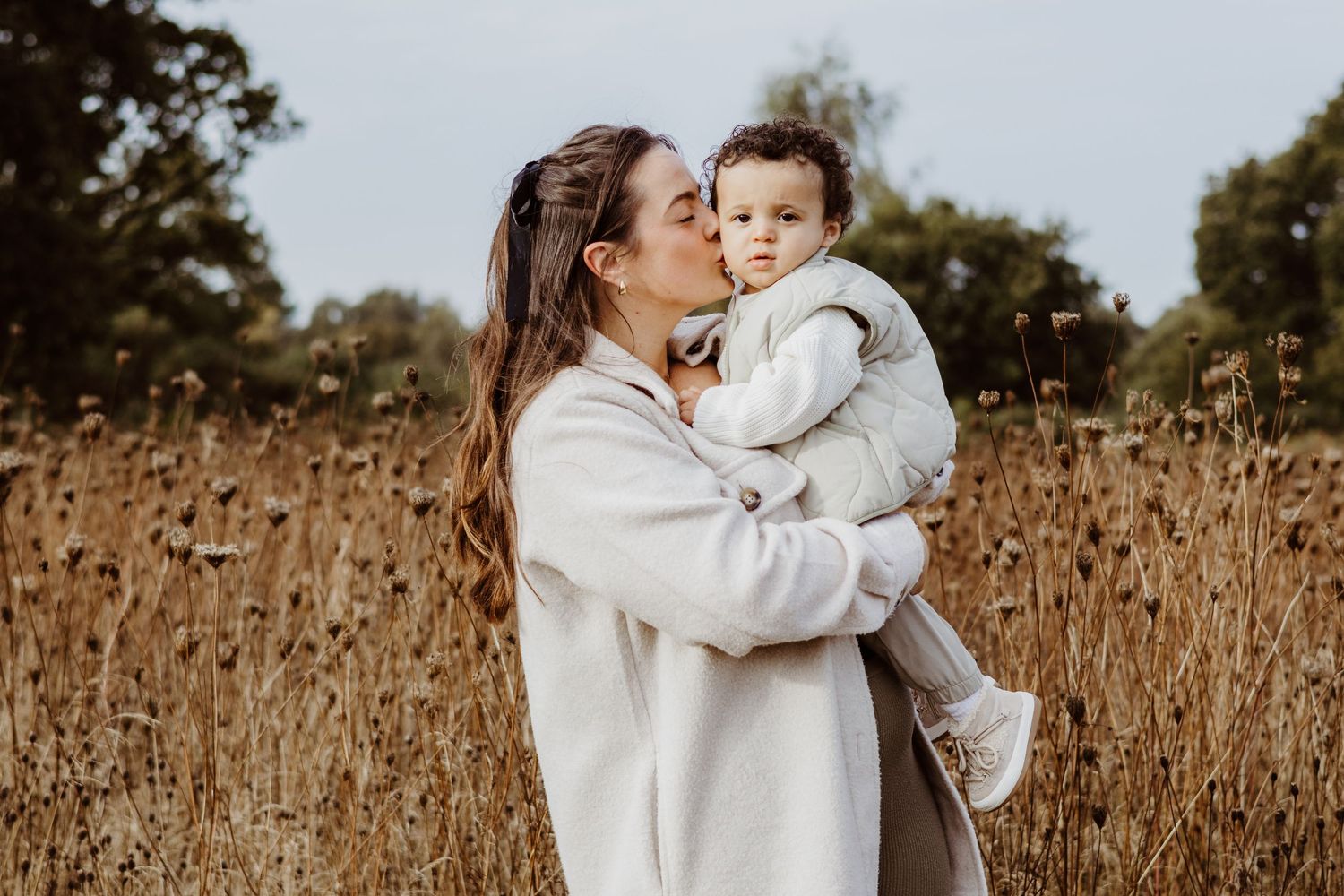 A sweet outdoor portrait showing affection between parent and child among tall autumn grasses.
