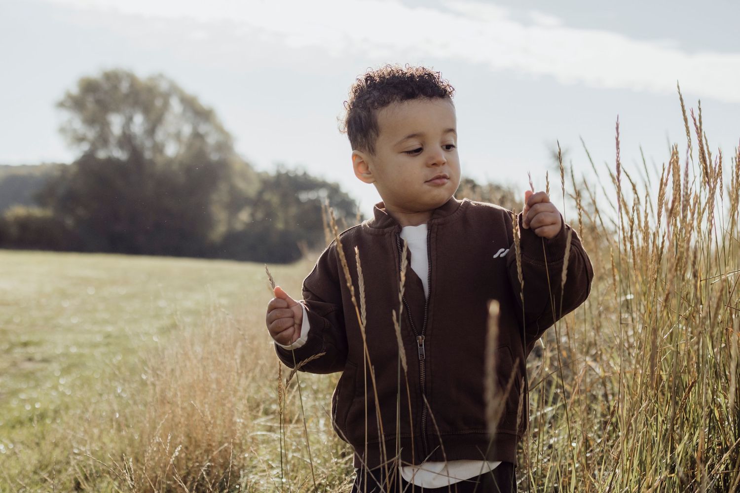 Child playing in tall grass during golden hour with sunlight illuminating the scene.