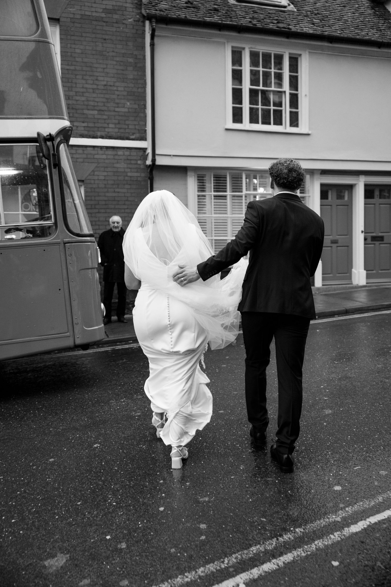 A couple walks down a wet street with the bride's dress flowing in the wind.