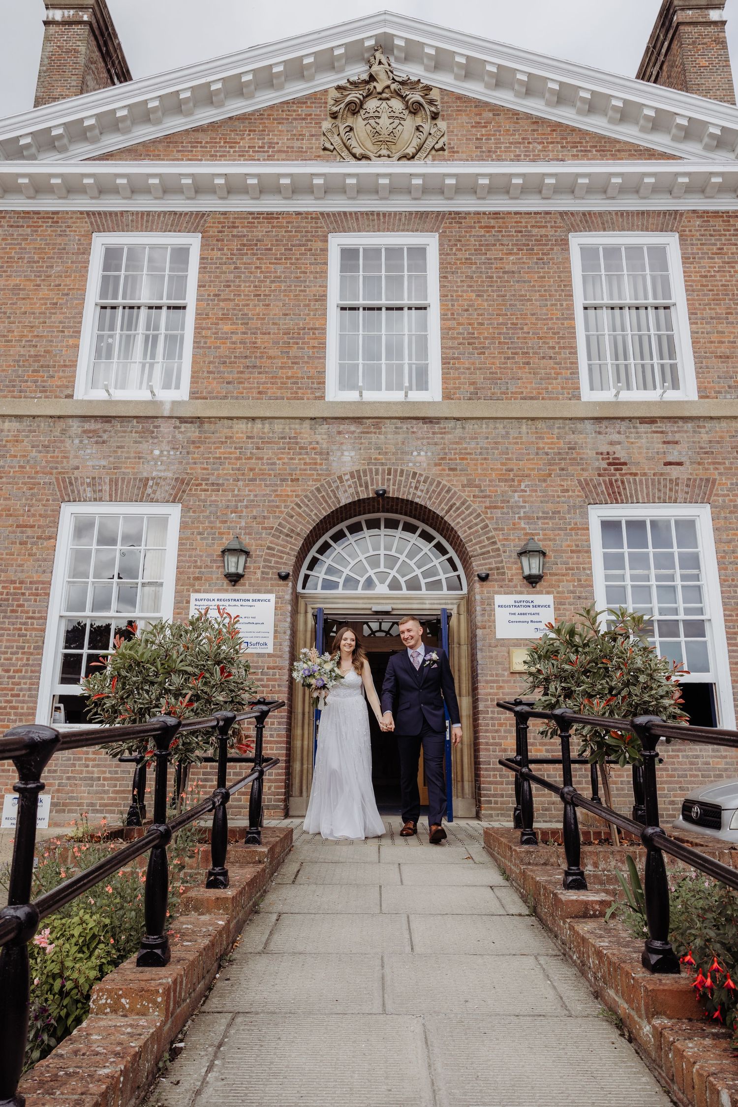 Elegant brick colonial style building with white trim and arched entrance serves as backdrop for outdoor wedding ceremony.