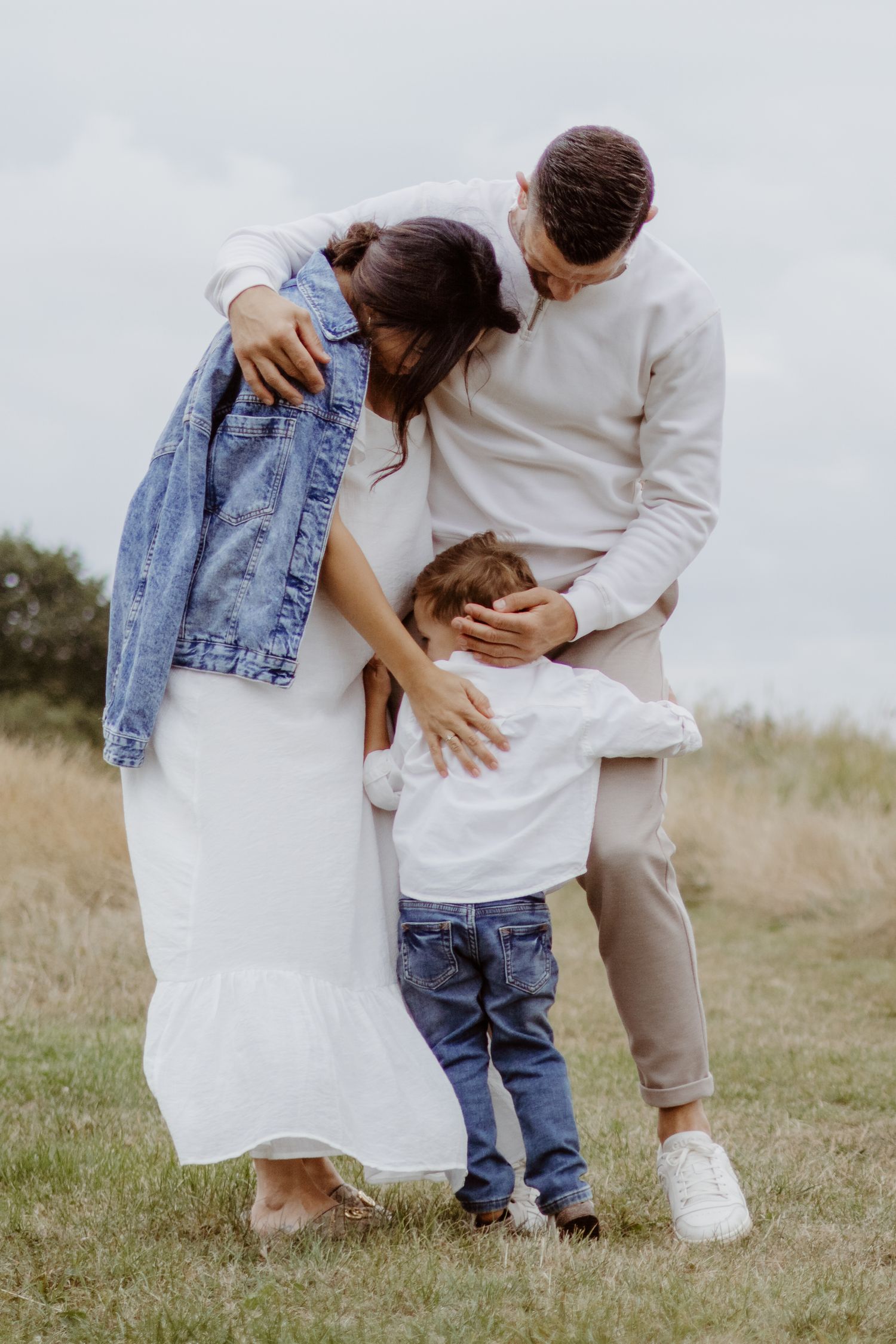 A family wearing coordinated white and denim outfits shares intimate moments in a grassy field.