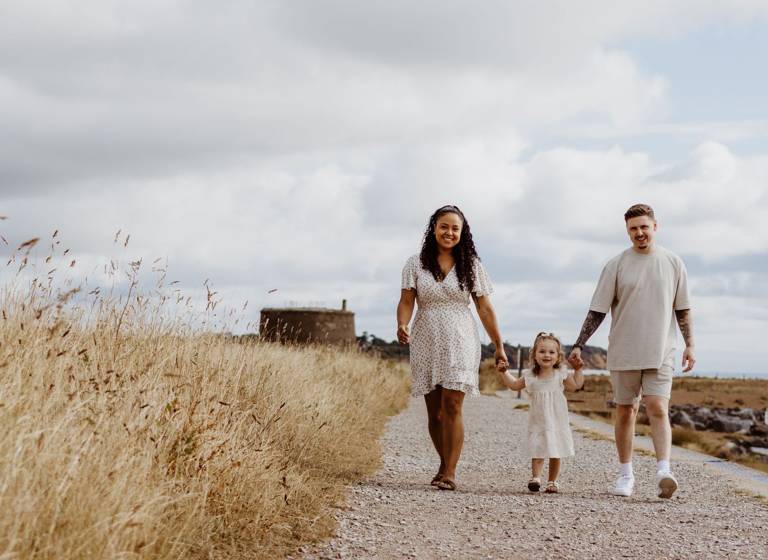 Family walks together on a scenic path through tall grass on a cloudy day.