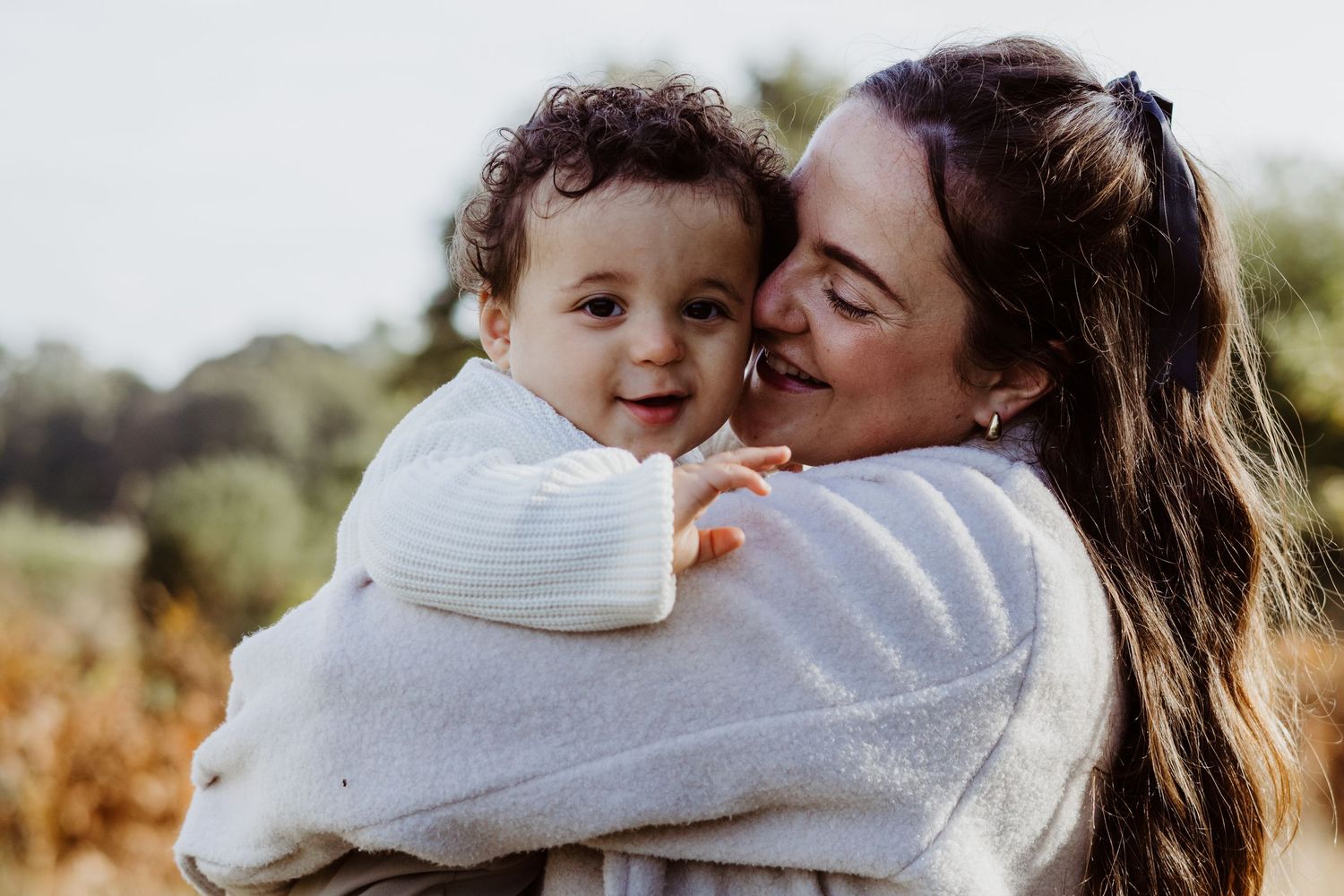 A heartwarming outdoor portrait showing a parent and child embracing in matching white sweaters.