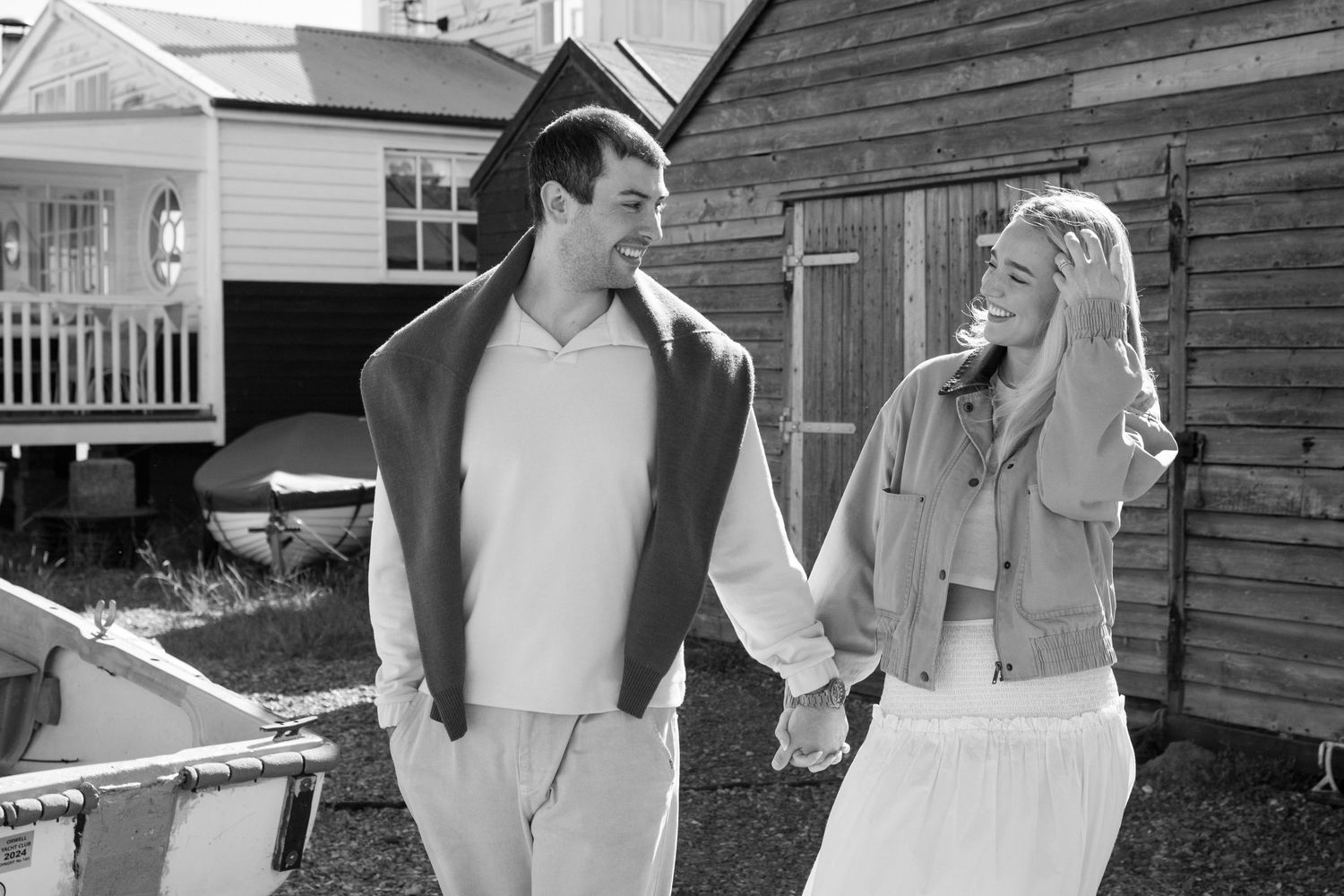 A black and white photograph shows two people in casual attire conversing outdoors next to a wooden building.