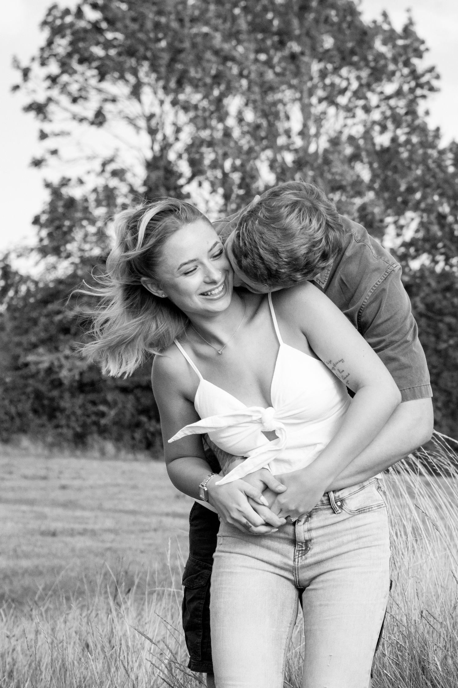 Couple sharing tender moment in sunlit field with natural backdrop.