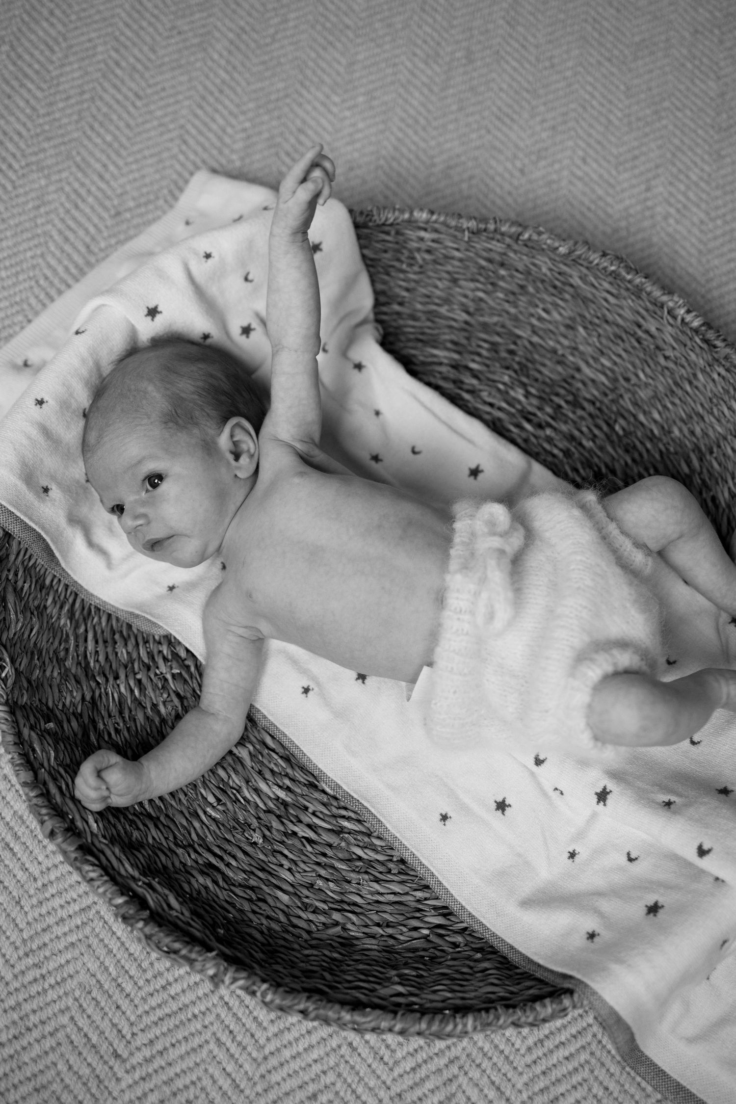 A sleeping baby wearing a star-printed onesie lies peacefully in a woven basket in black and white.
