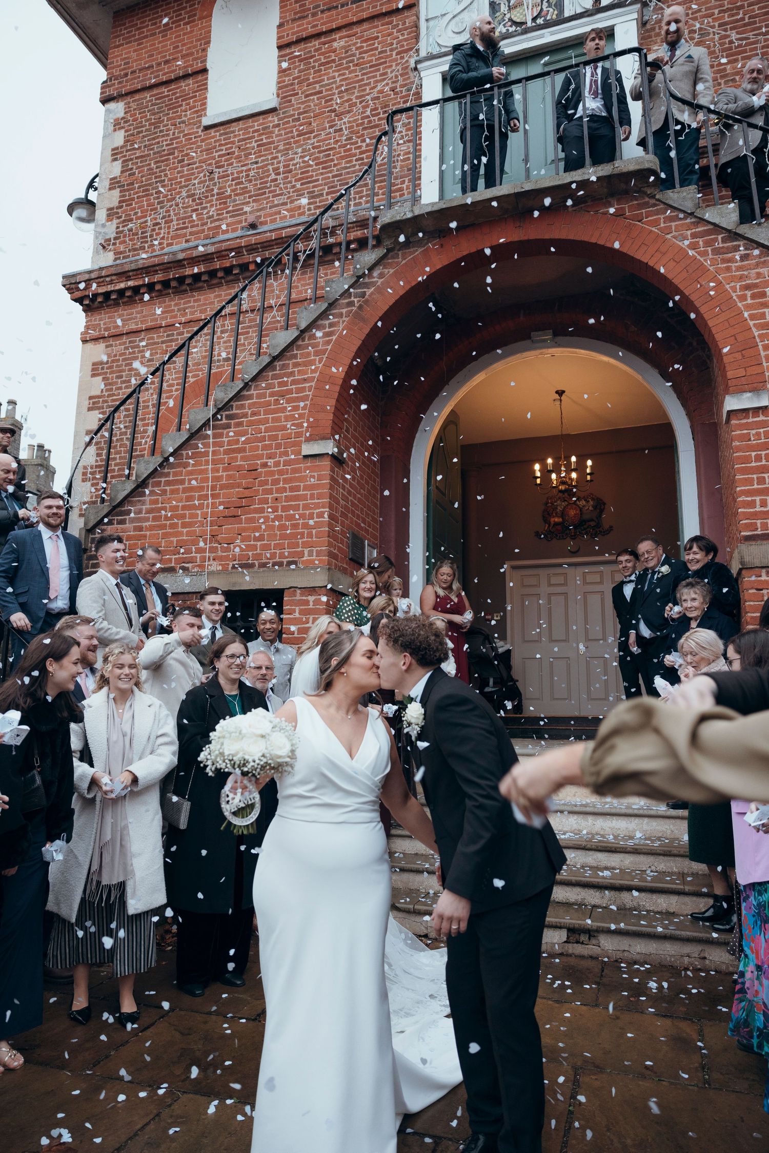 Wedding exit celebration with confetti outside a historic brick building.