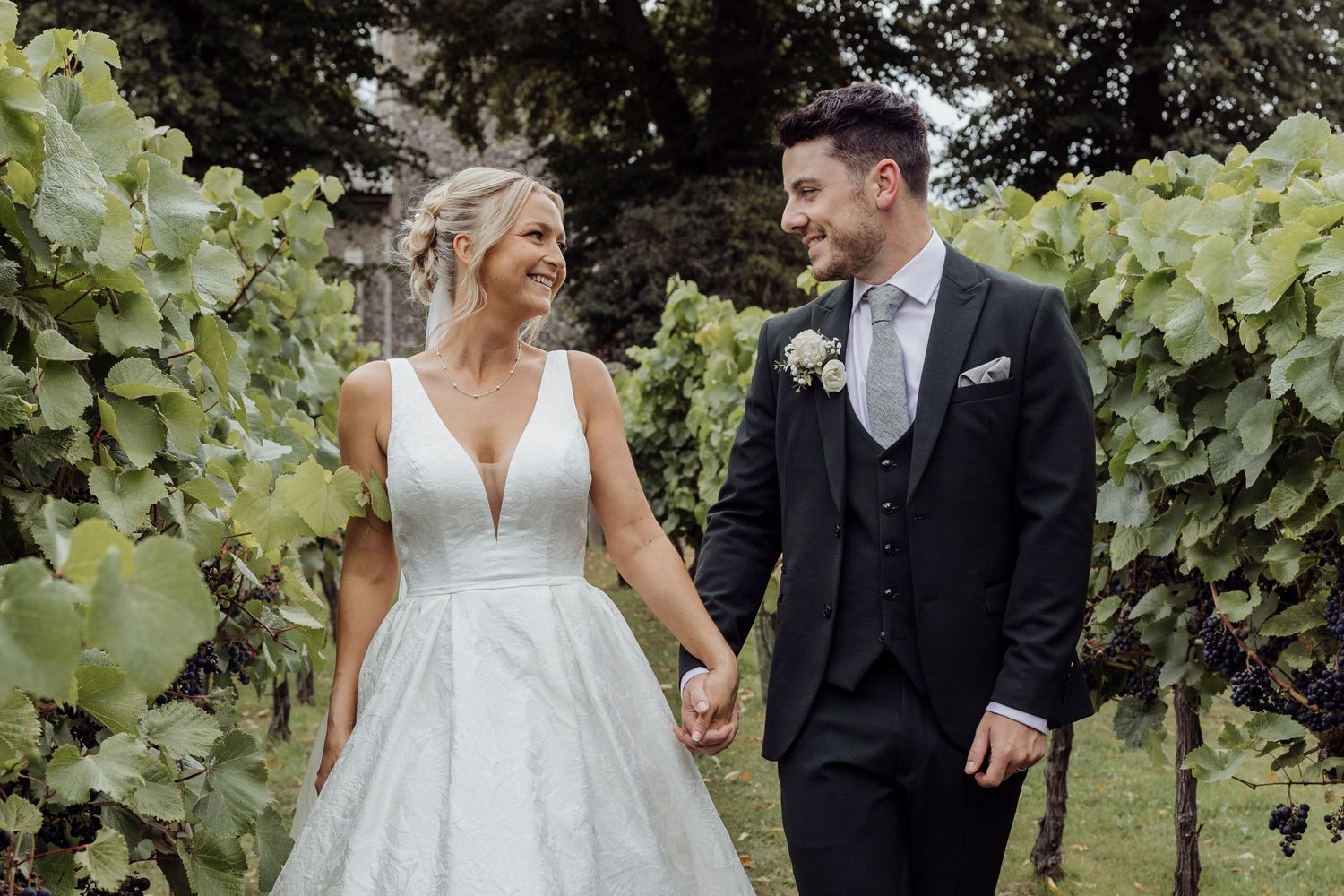 Newlyweds share a joyful moment while holding hands in a lush vineyard setting.
