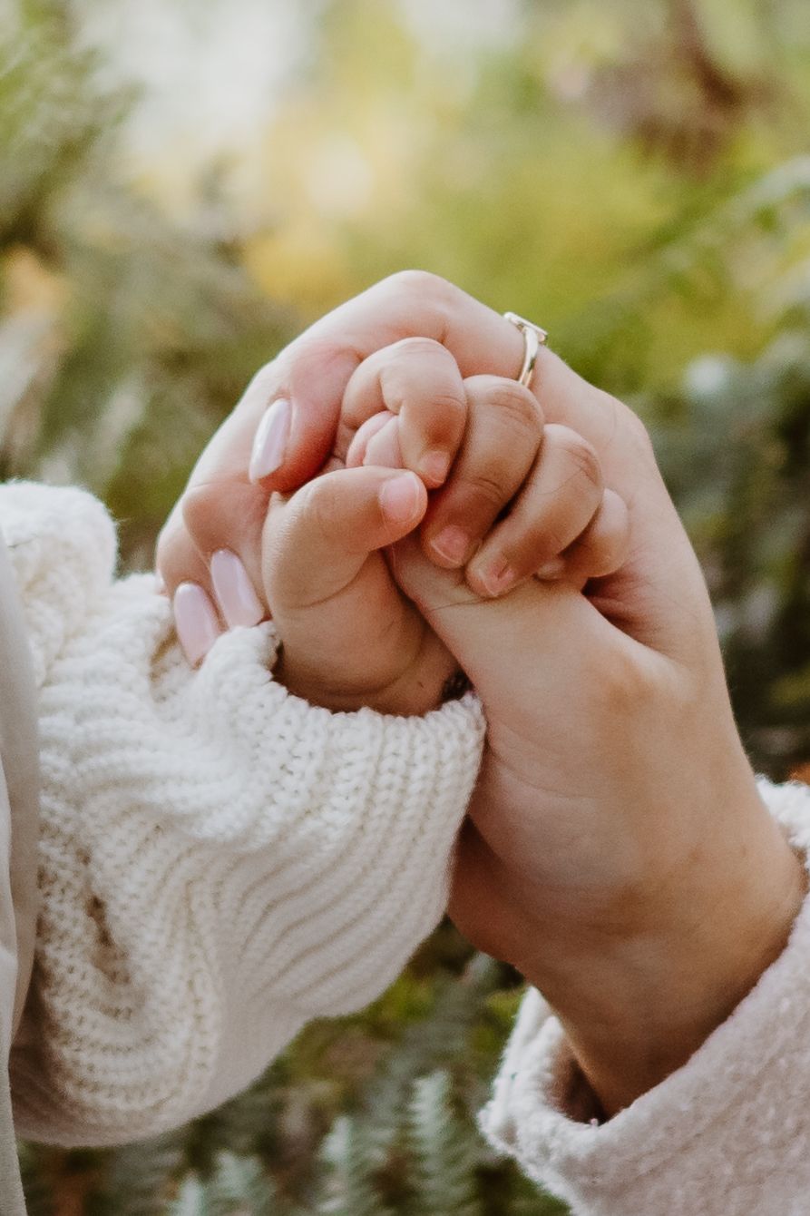 A close-up photograph of adult and baby hands tenderly clasped together showing a delicate ring.
