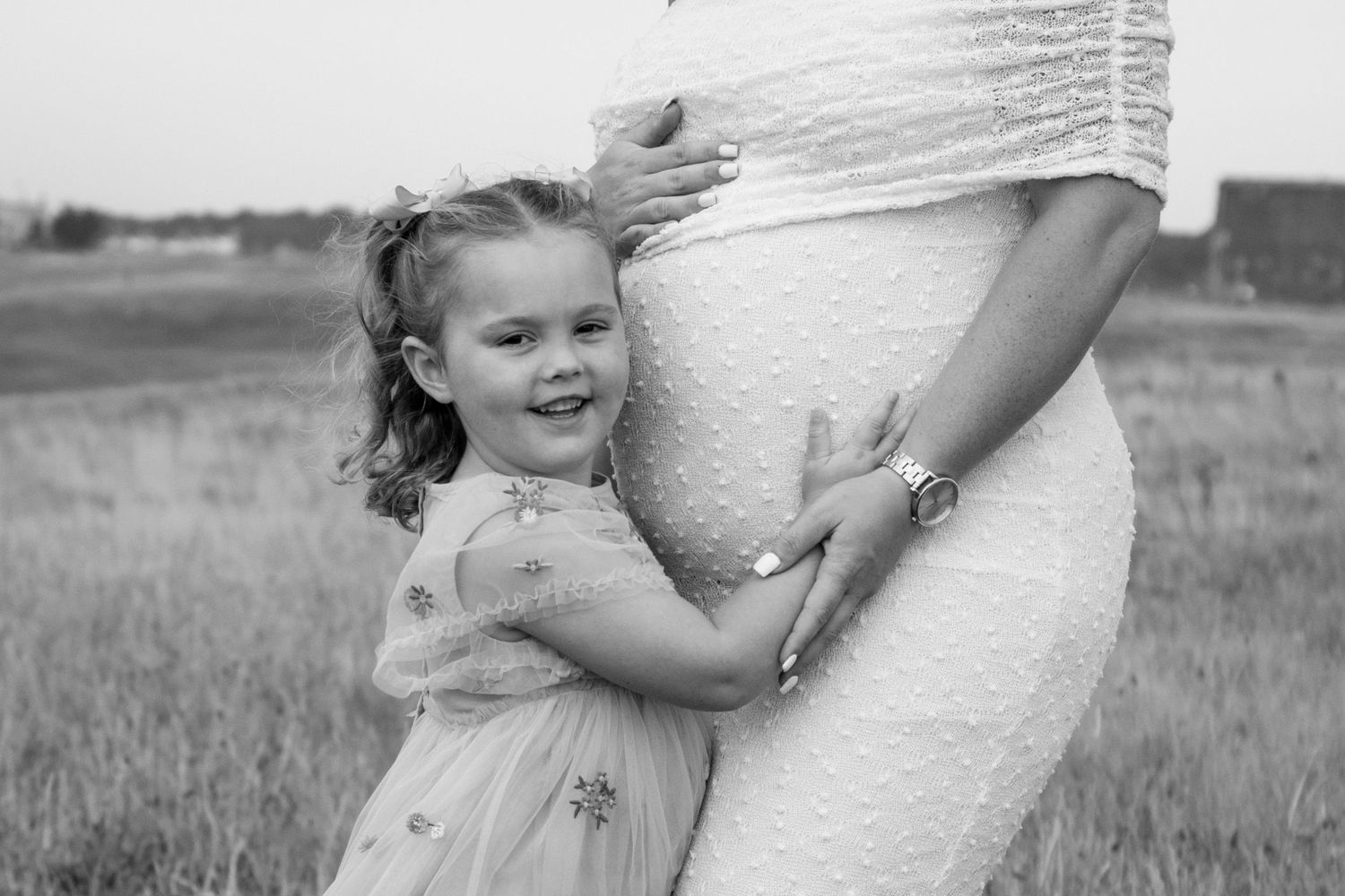 Black and white photo series showing tender moments between a child and parent in a grassy field.