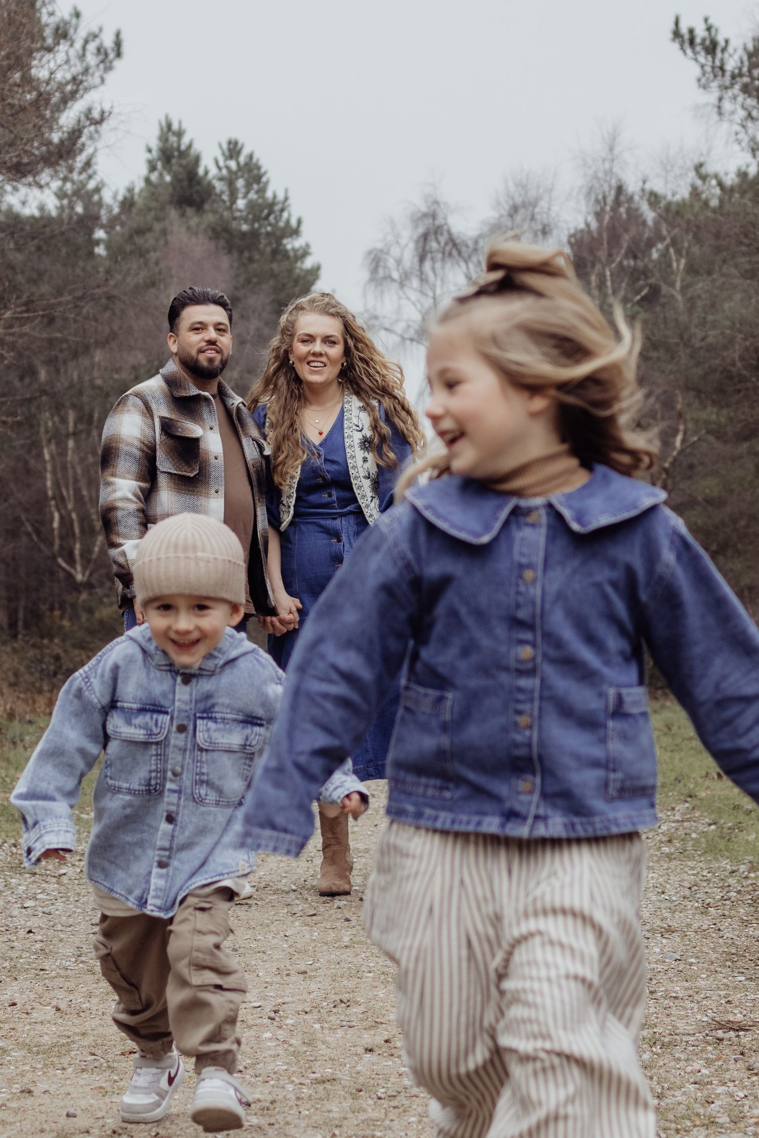 Children playing and running on a trail wearing matching denim jackets and striped pants.