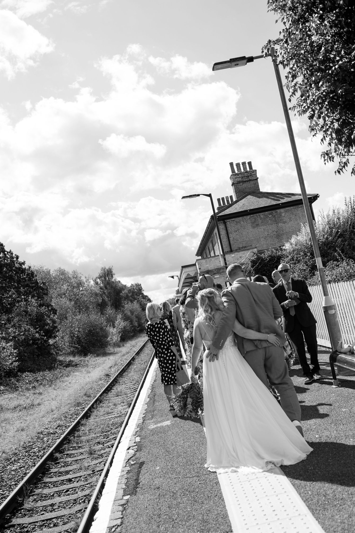 A wedding party poses for photos along rustic train tracks on a sunny day.