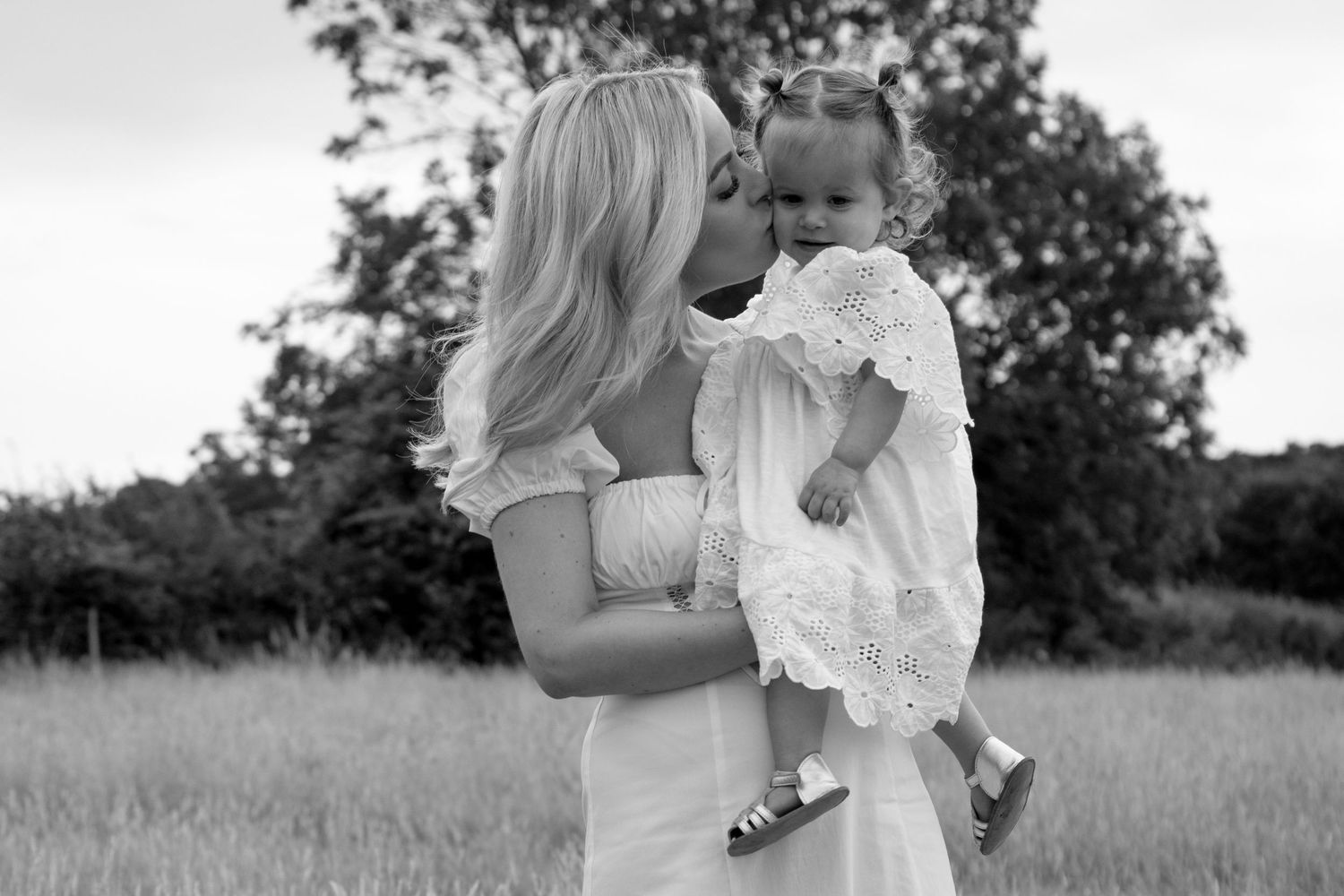 Family dressed in white embraces while standing in a sunlit natural outdoor setting.