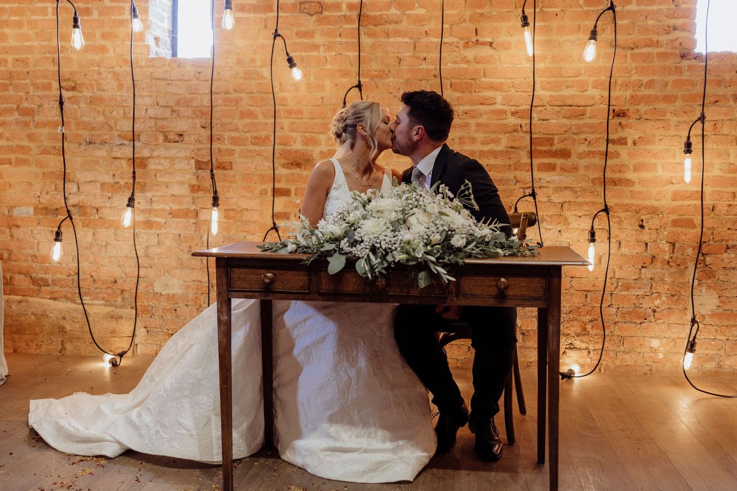 A romantic scene with string lights and exposed brick walls at an indoor wedding venue.