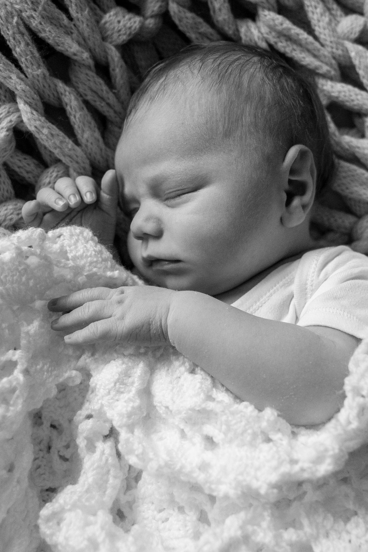 A sleeping baby rests peacefully on white lace bedding in a black and white photograph.