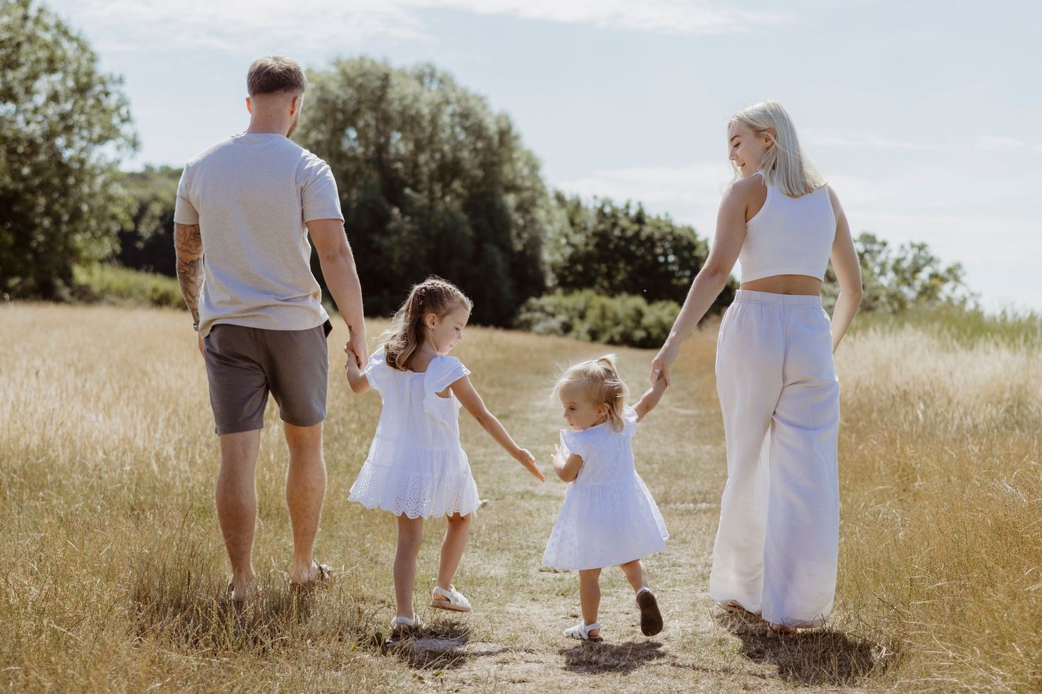 Family walking together through a sunlit meadow in matching white outfits.