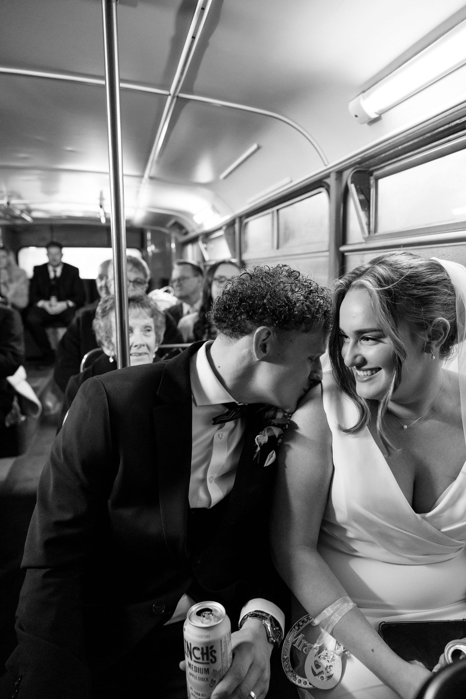 A candid moment captured on a vintage bus between newlyweds holding drinks.